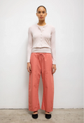 Woman wearing a white top and coral pants against a plain background