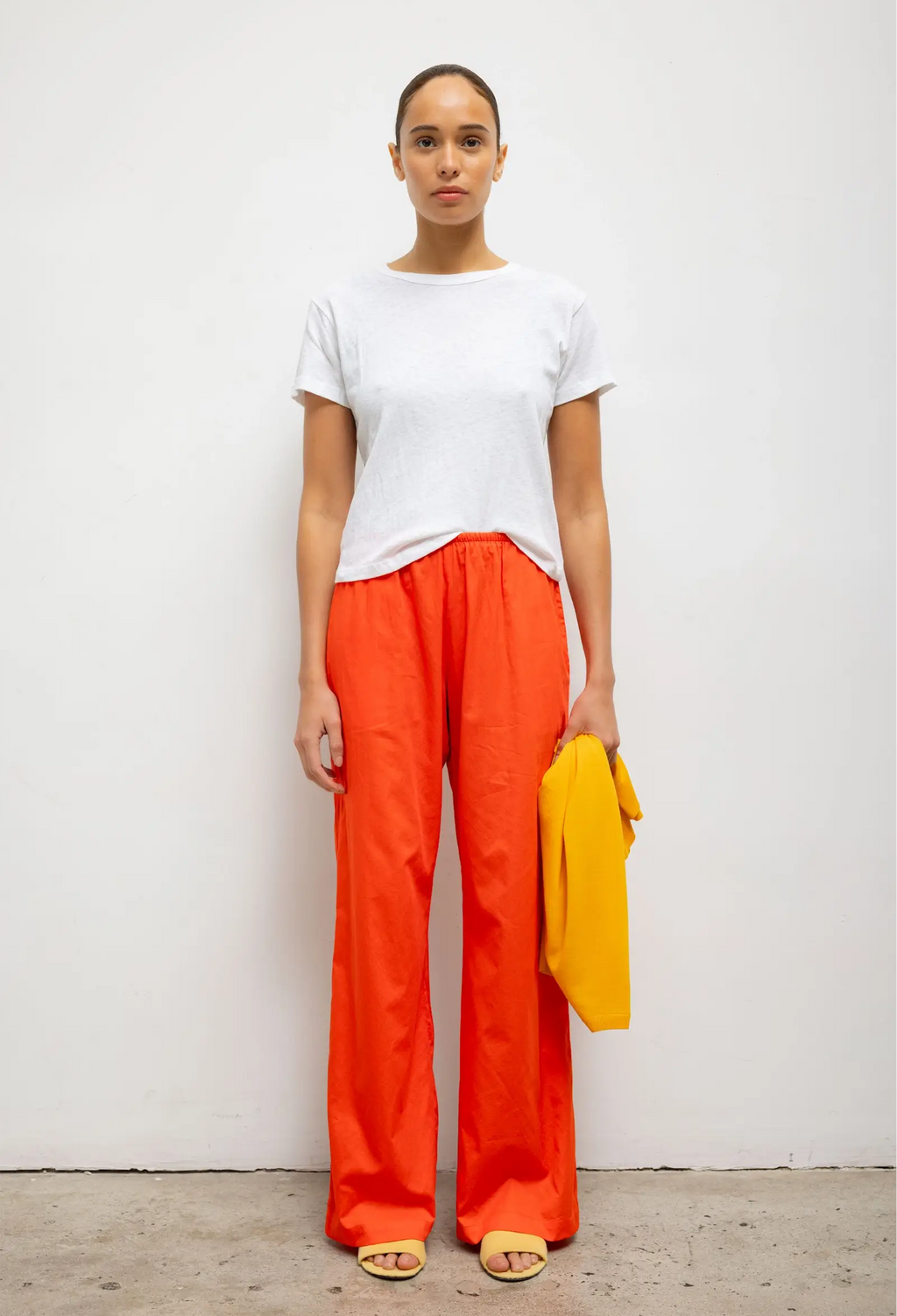 Person wearing a white top and bright orange pants against a white background