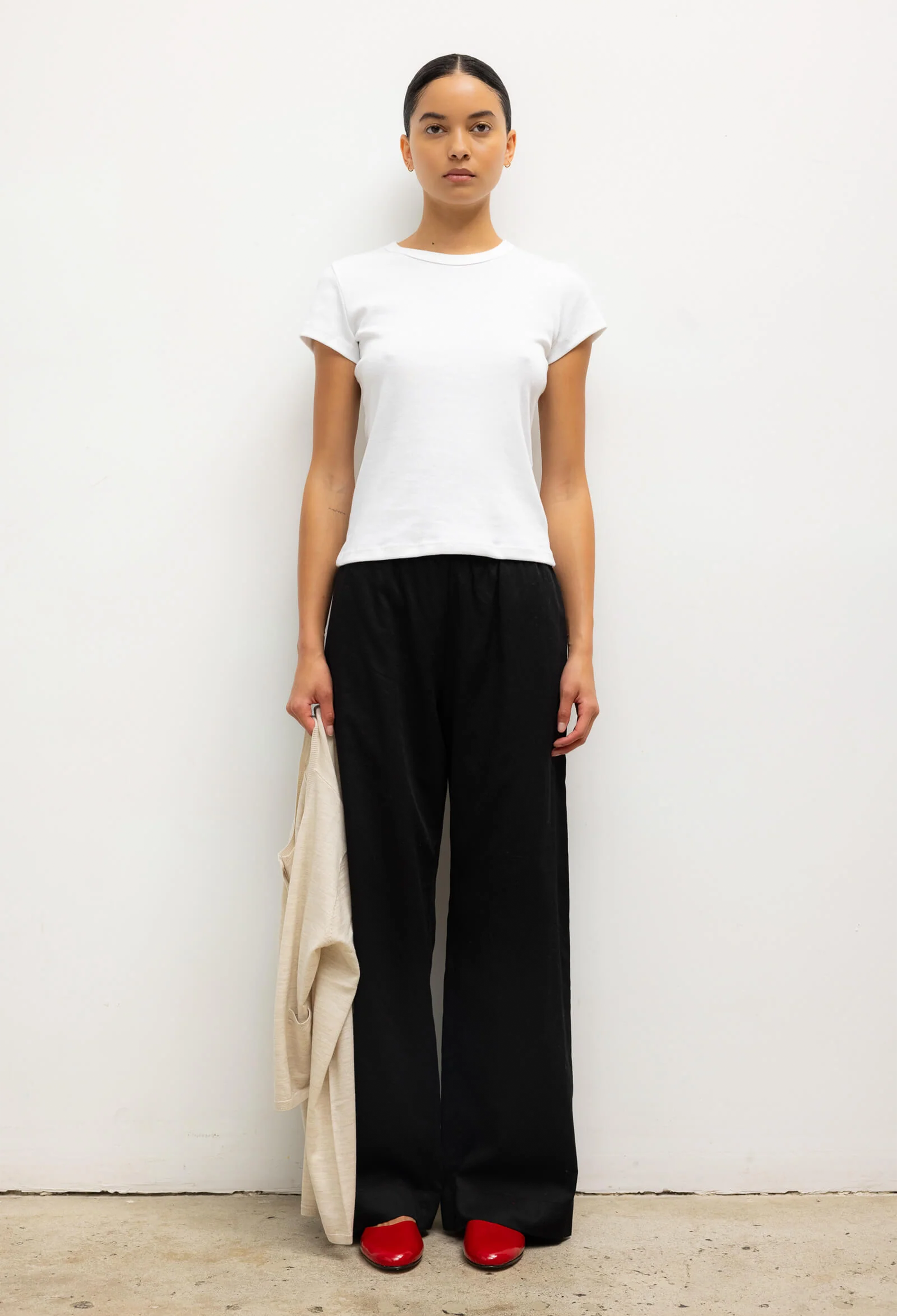Person wearing a white top and black pants against a white background