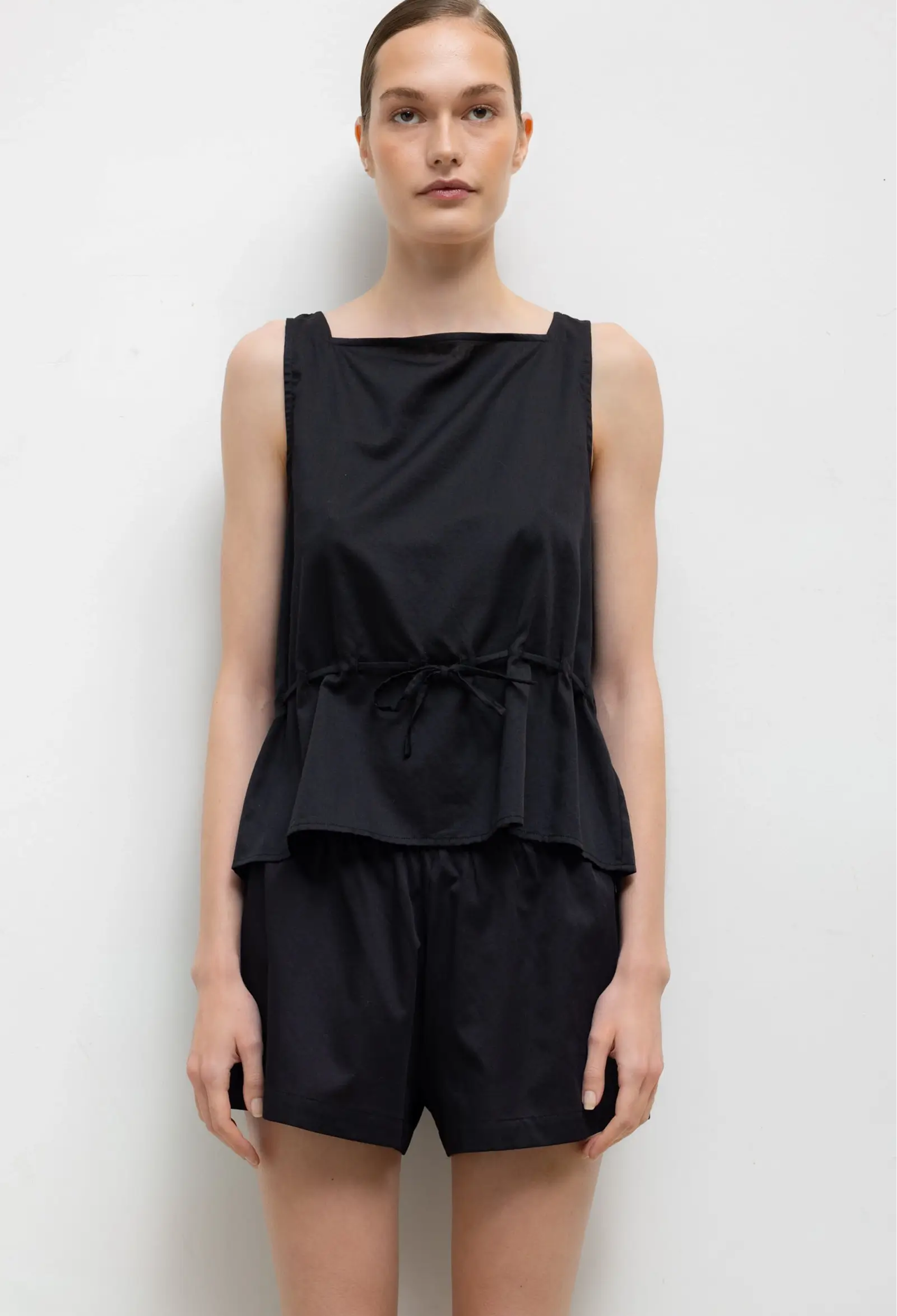Woman wearing a black sleeveless top and shorts on a white background
