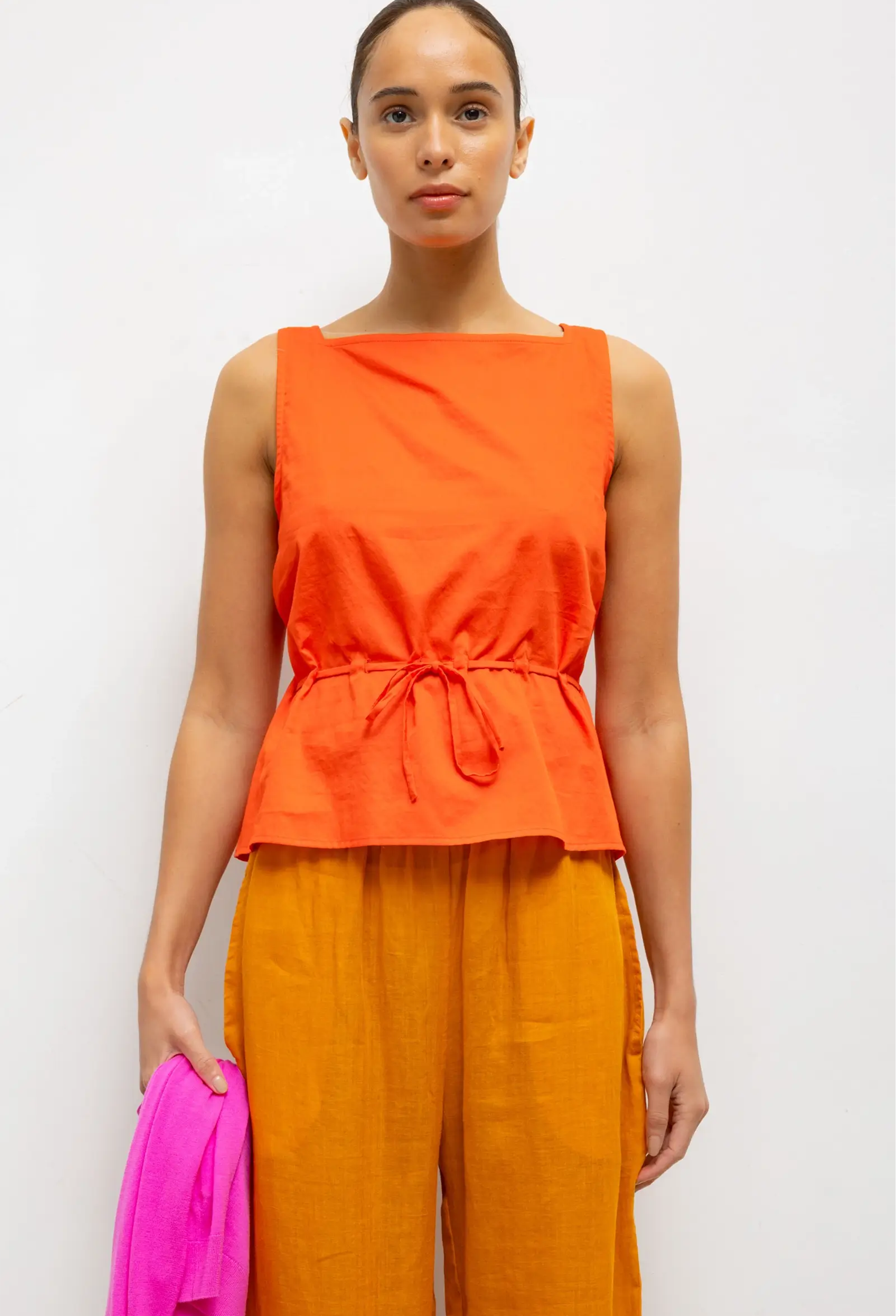Woman wearing an orange sleeveless top and orange pants against a white background