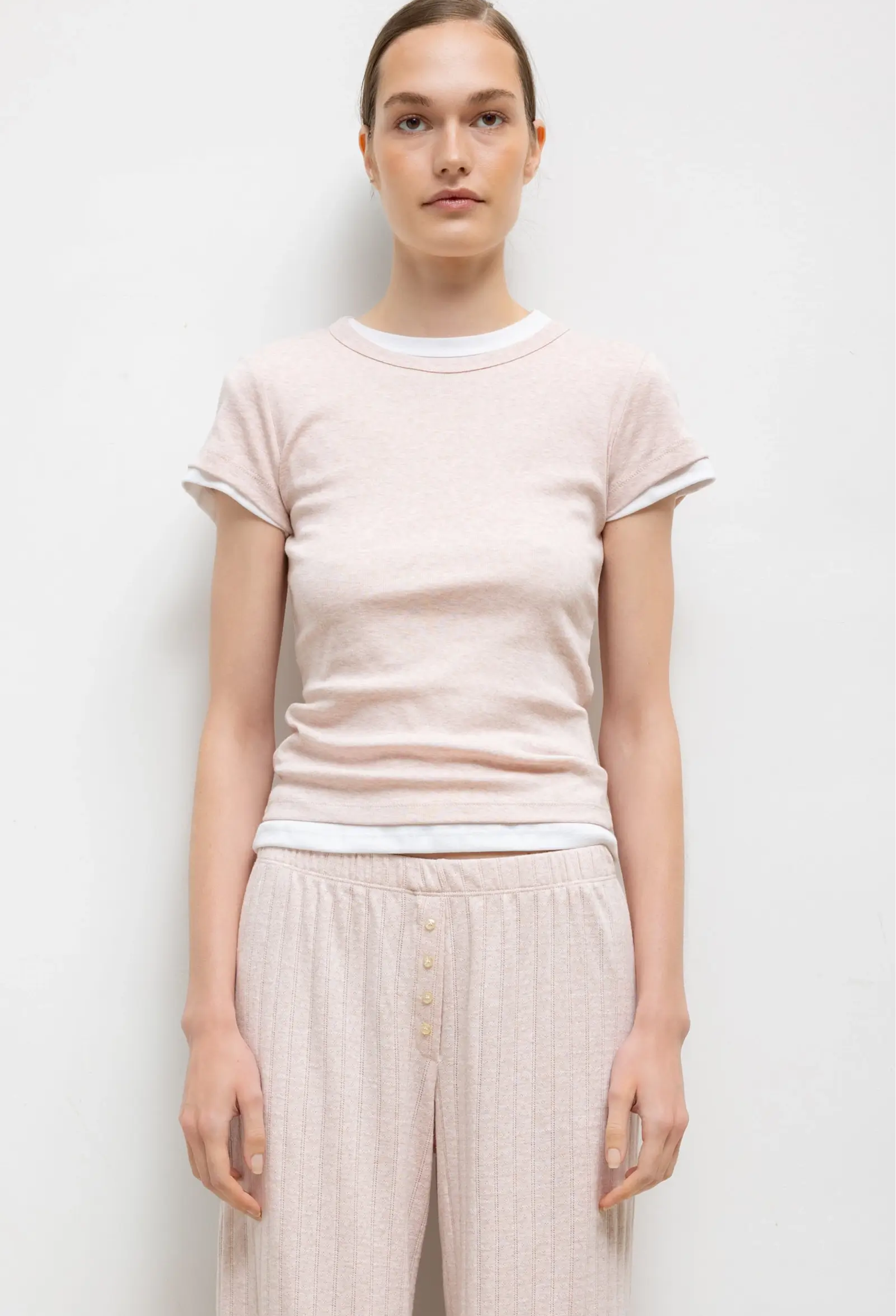 Person wearing a light pink t-shirt and beige pants on a white background