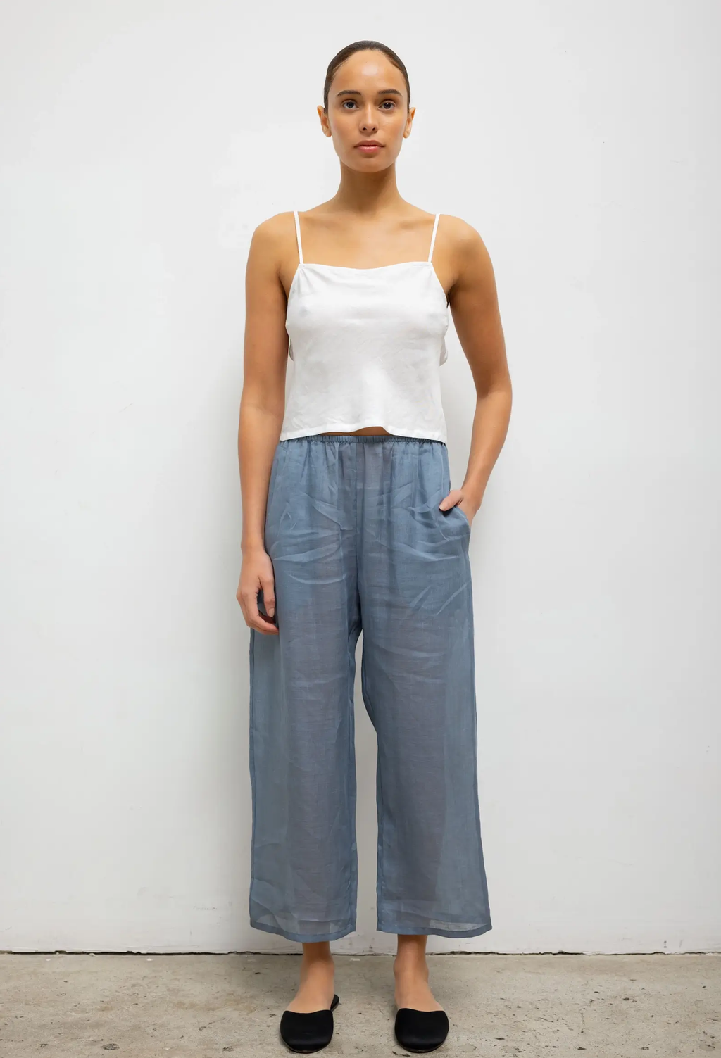 Woman wearing a white top and blue pants against a plain background