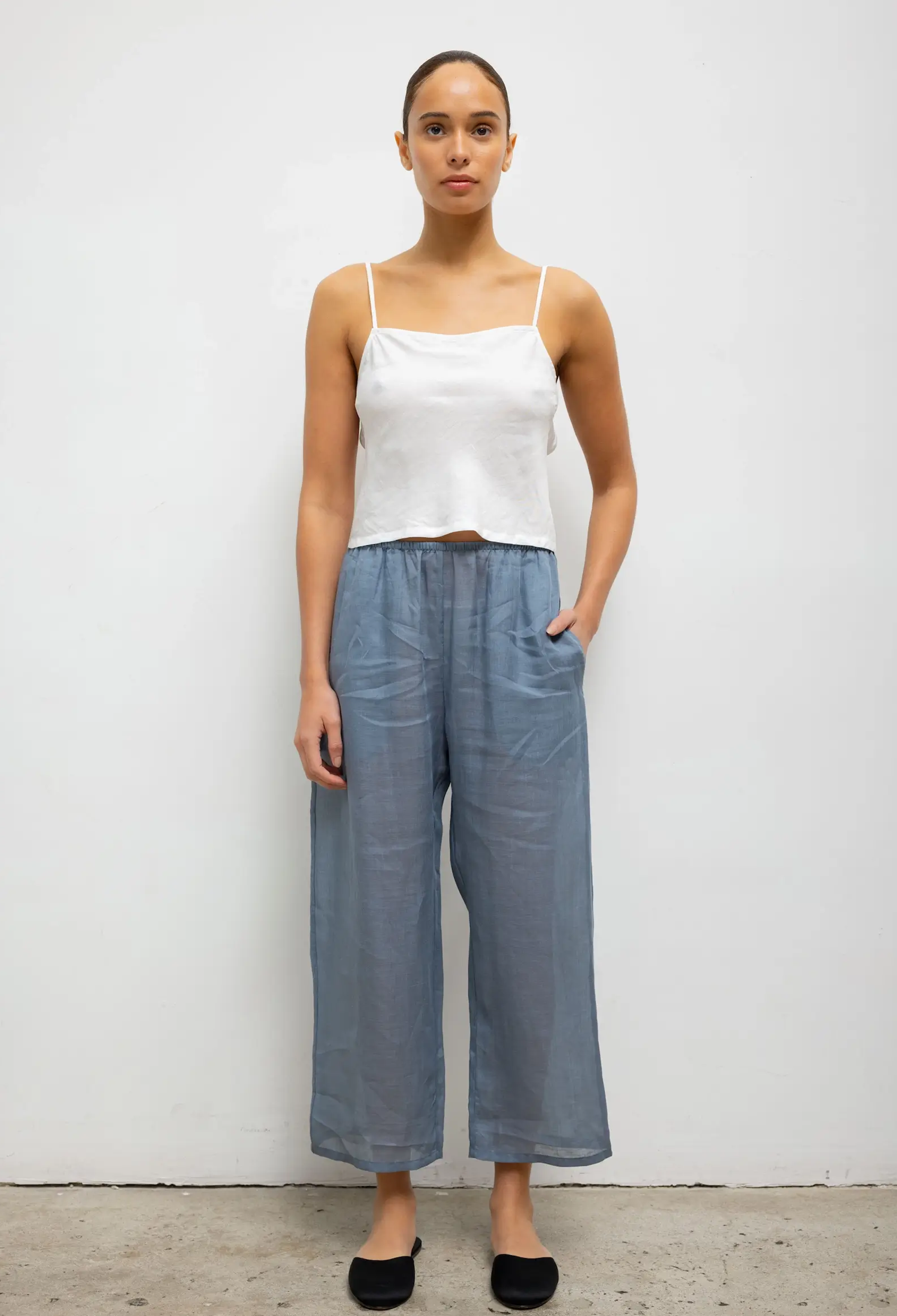 Woman wearing a white top and blue pants against a plain background