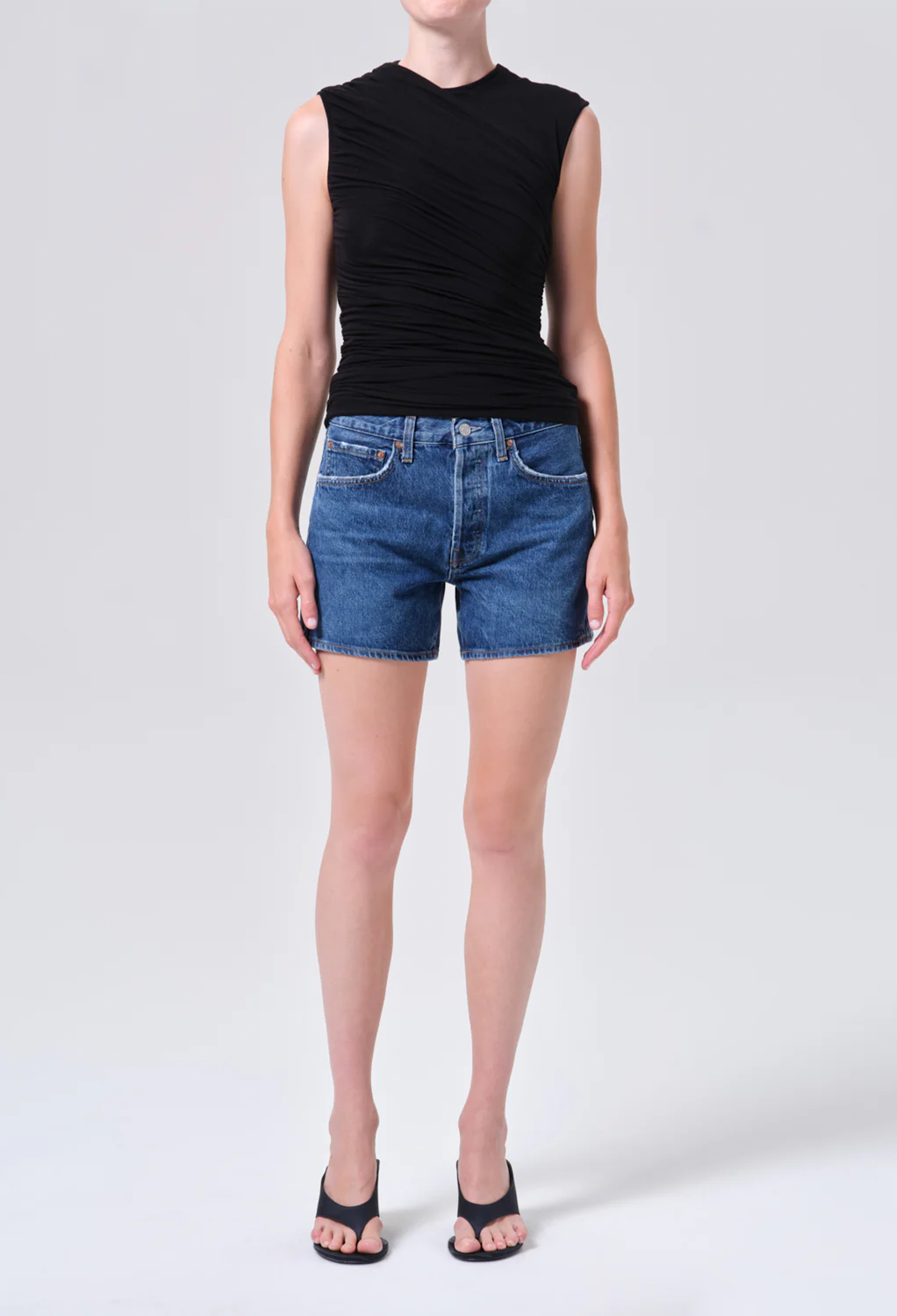 Person wearing a black sleeveless top and blue denim shorts on a white background