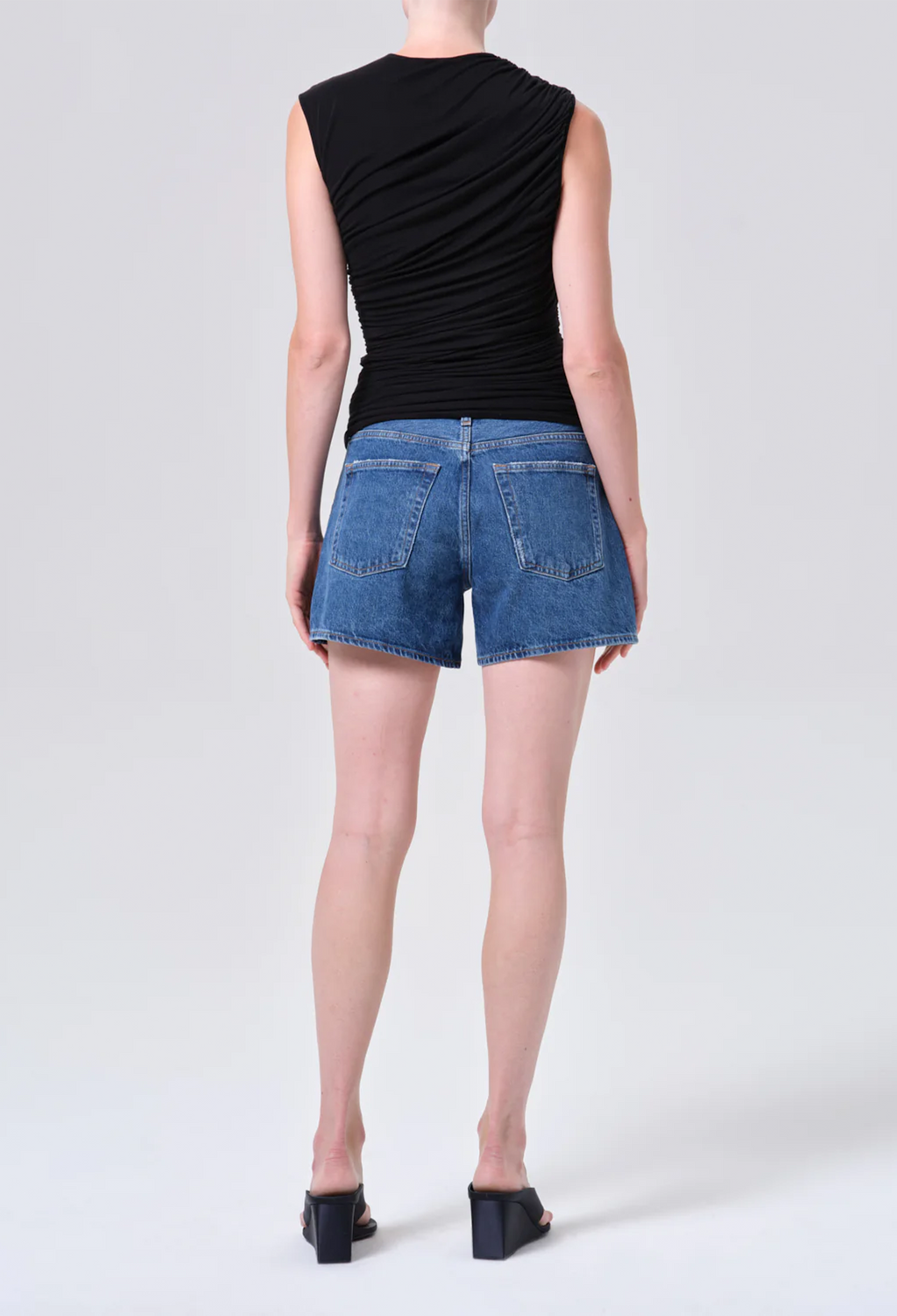 Person wearing a black sleeveless top and blue denim shorts on a white background