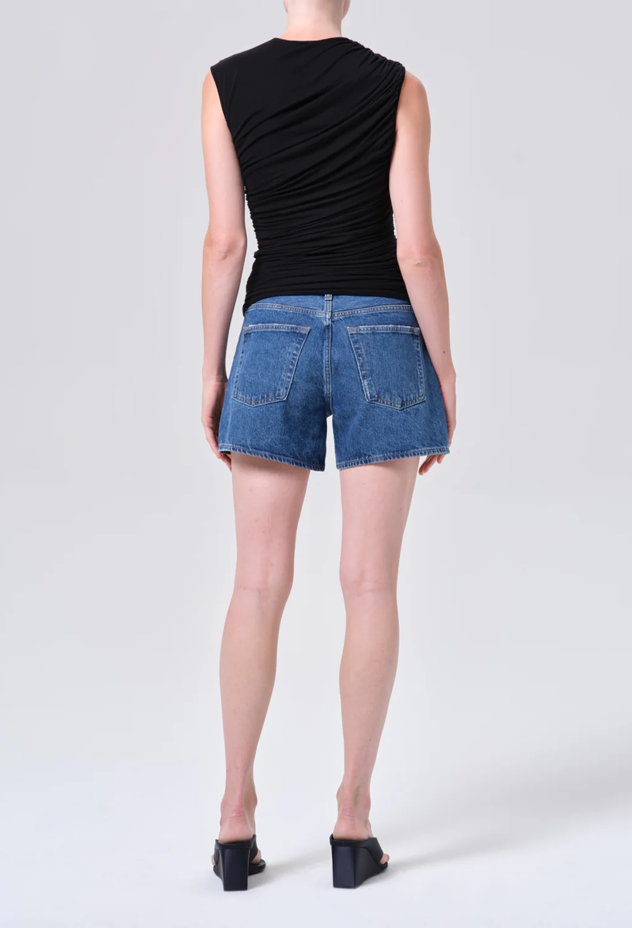 Person wearing a black sleeveless top and blue denim shorts on a white background