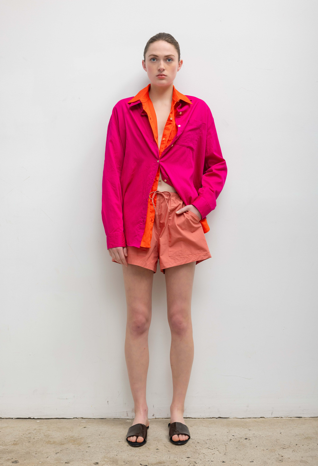 Person wearing a bright pink jacket with orange lining and peach shorts against a white background