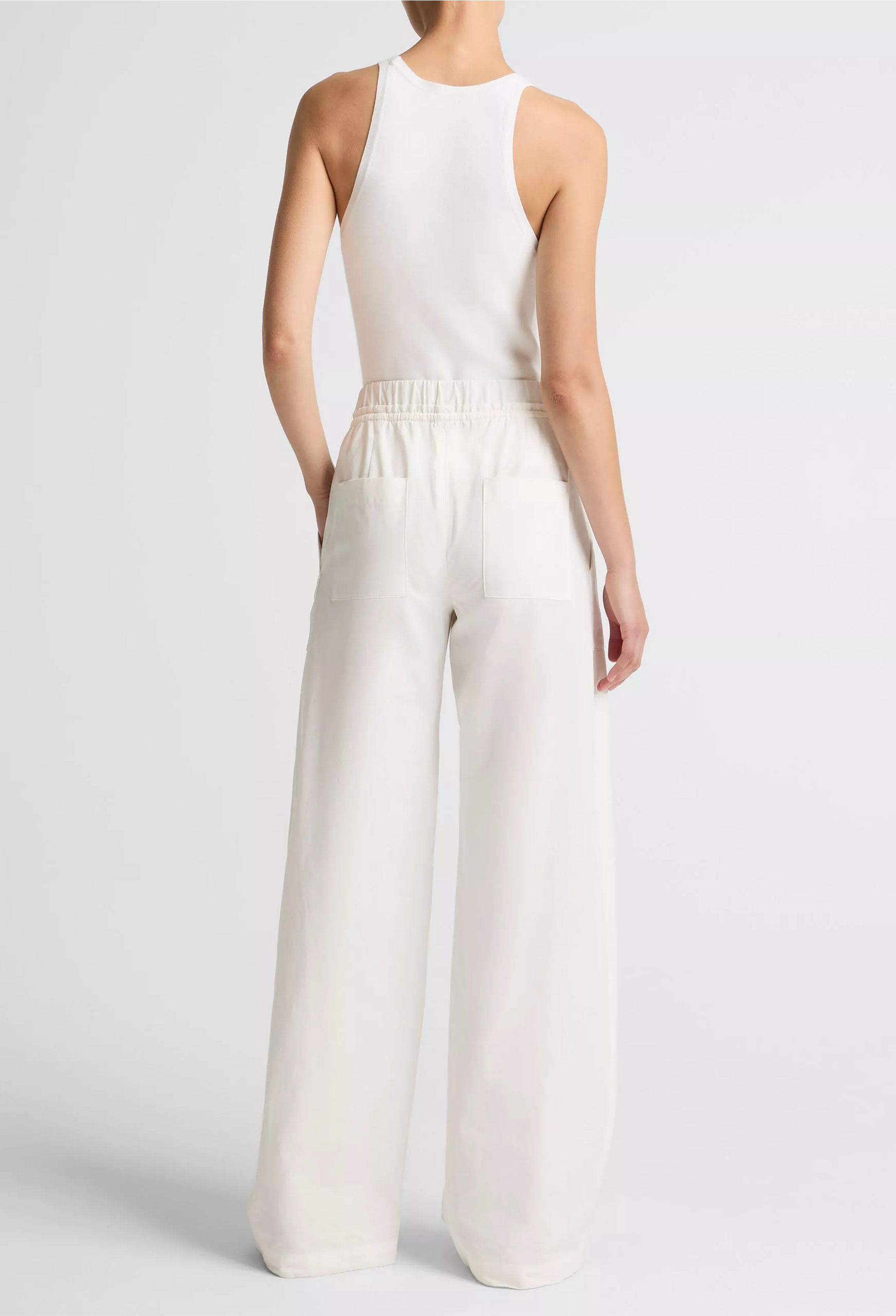 Person wearing a white sleeveless top and wide-leg pants on a light gray background