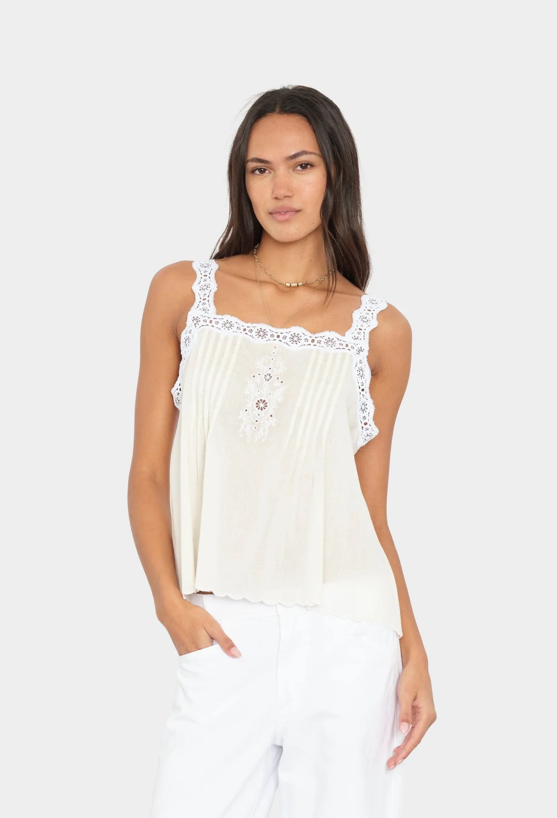 Woman wearing a white sleeveless top with lace details on a white background
