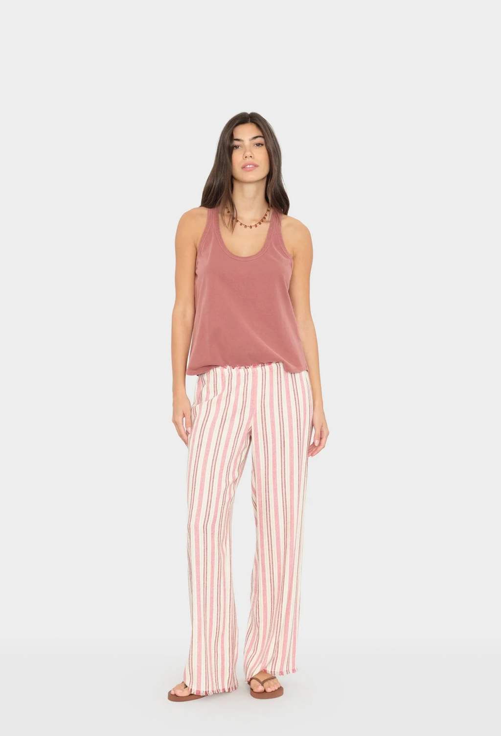 Woman wearing a mauve tank top and pink striped pants on a white background
