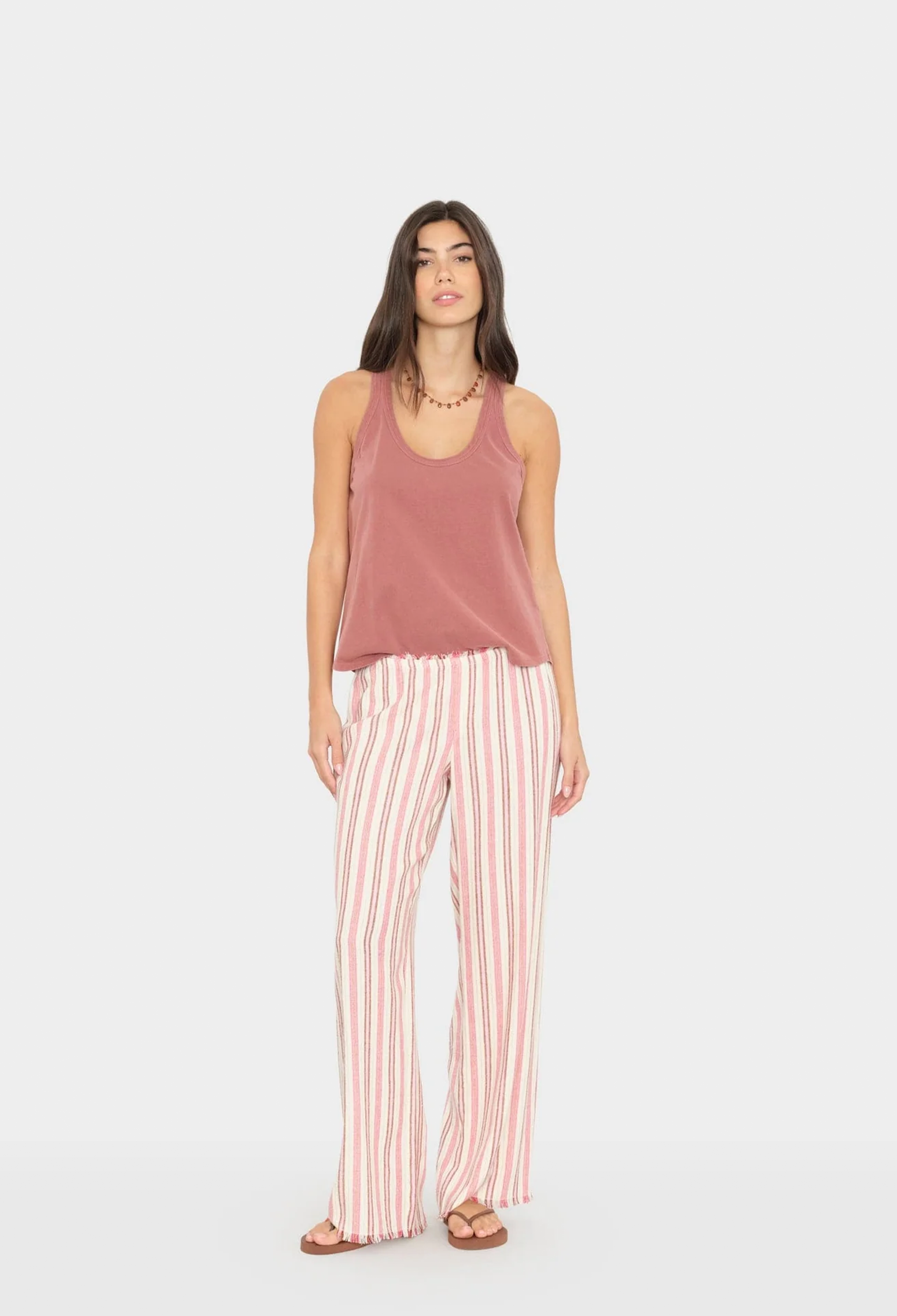 Woman wearing a mauve tank top and pink striped pants on a white background