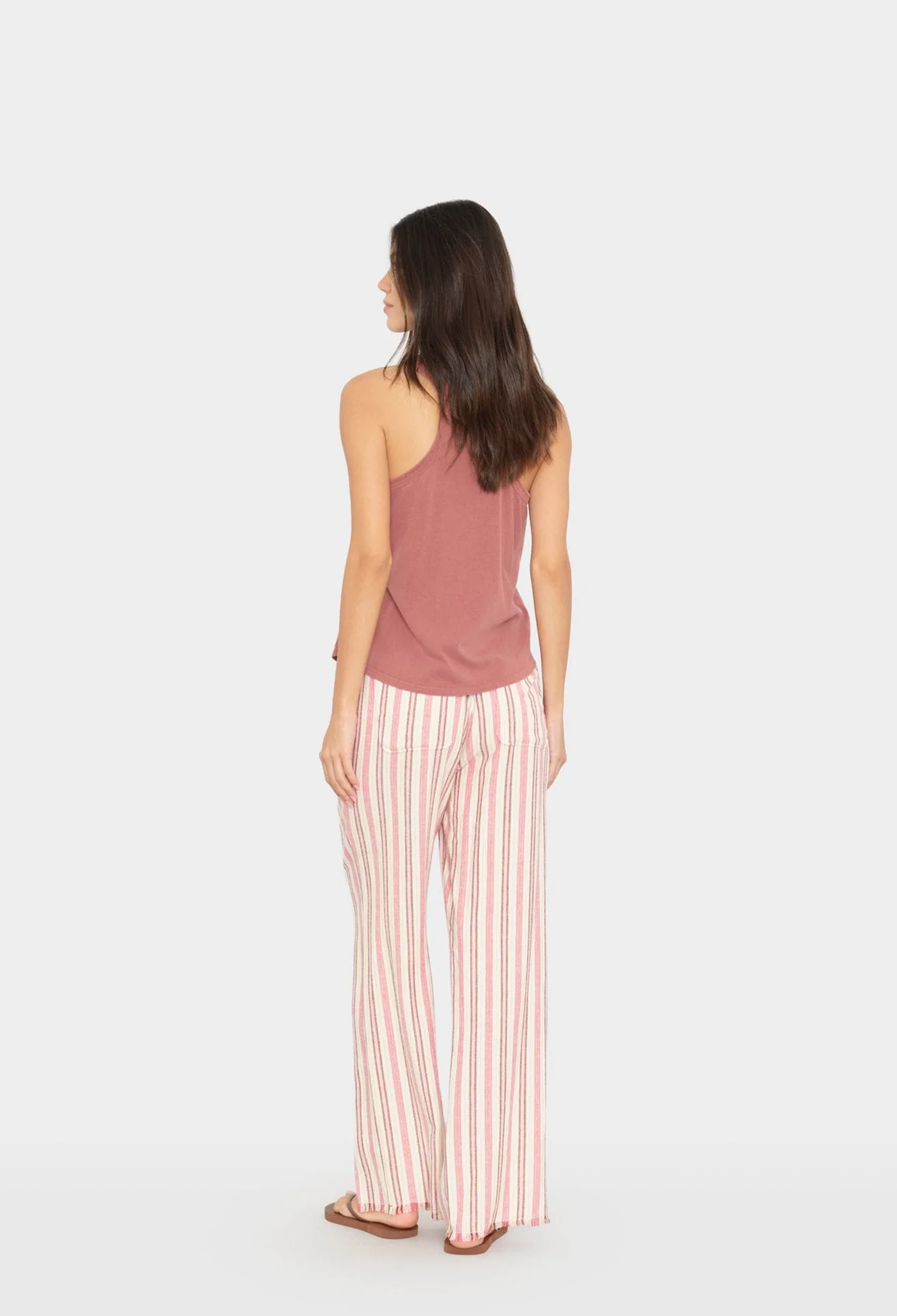 Woman wearing a pink sleeveless top and striped pants on a white background