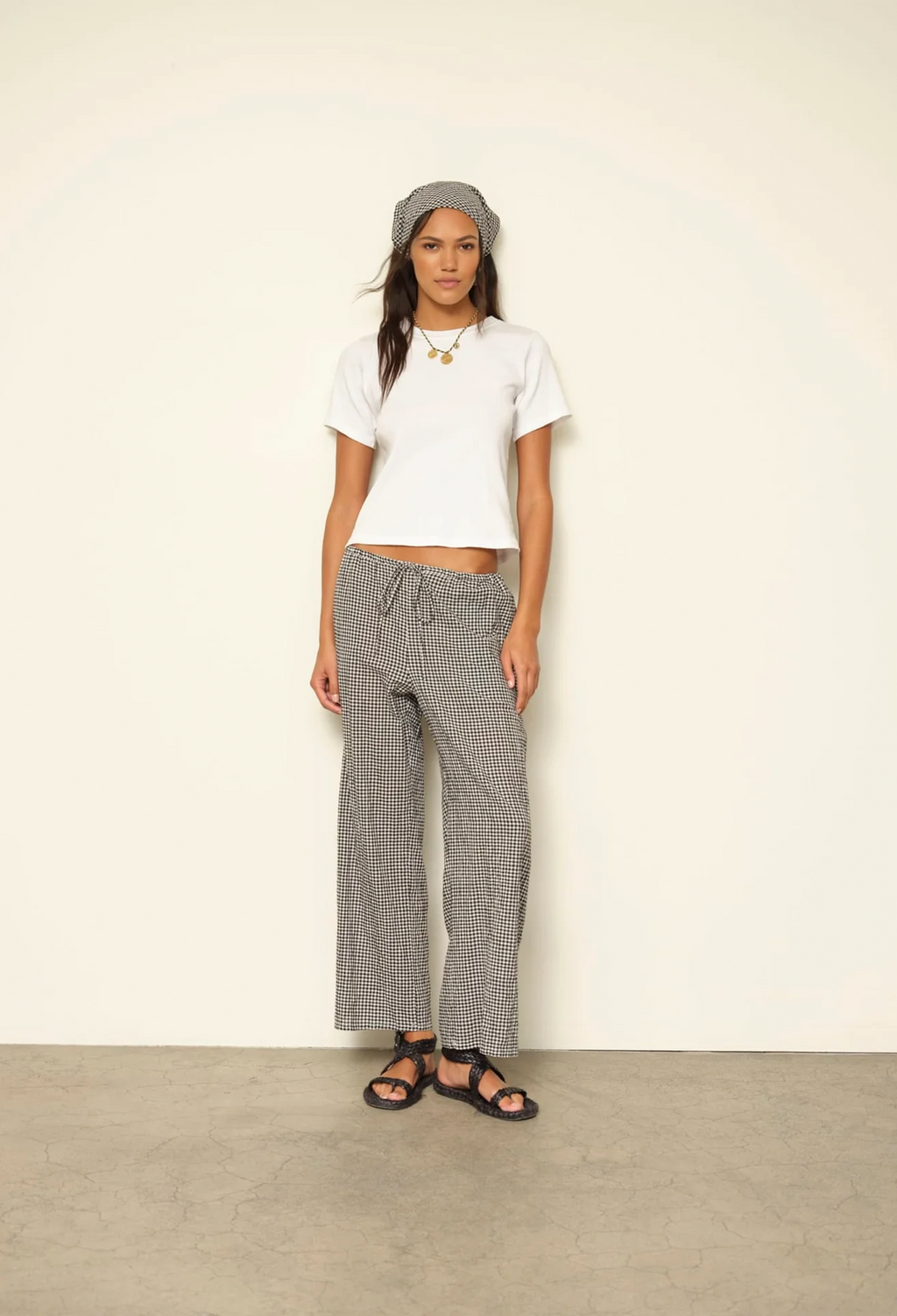 Woman wearing a white top and black checkered pants against a plain background