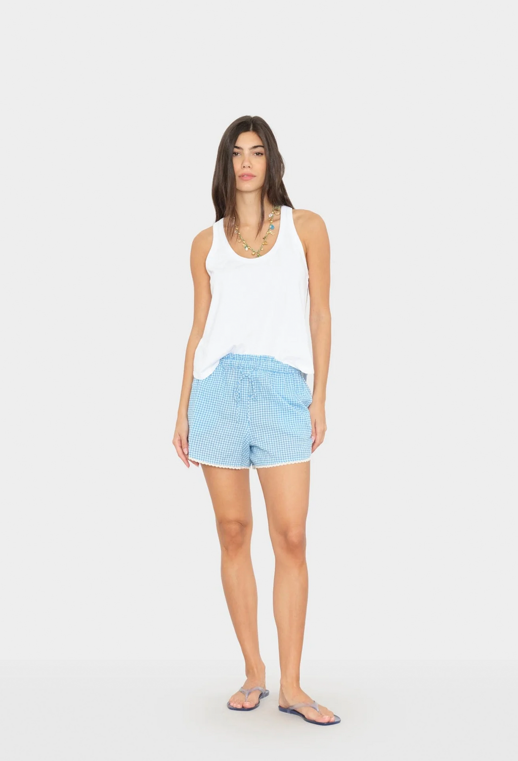 Woman wearing a white tank top and light blue shorts on a white background