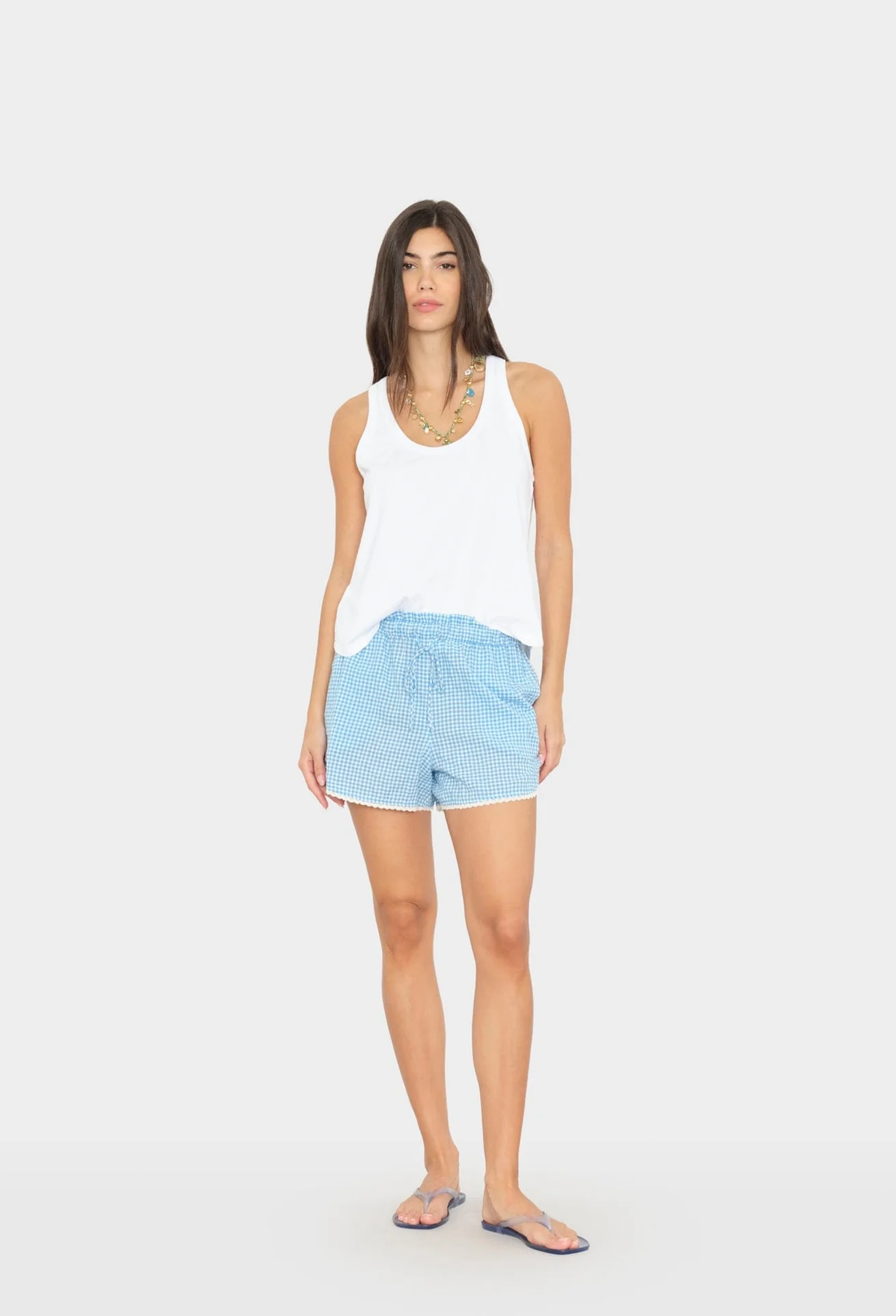 Woman wearing a white tank top and light blue shorts on a white background