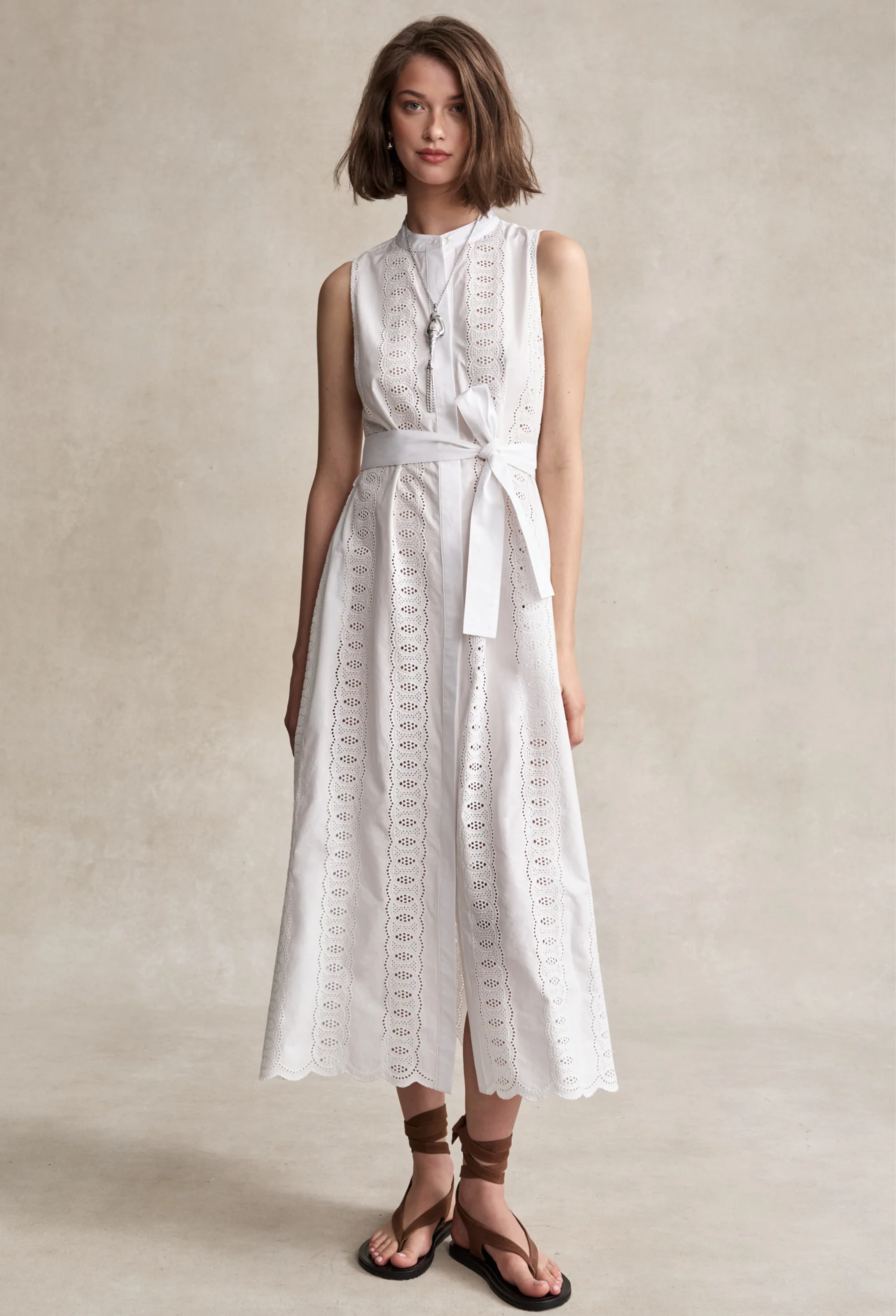 Woman wearing a white sleeveless dress with lace details on a beige background