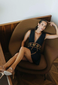 Woman in a black dress sitting on a brown chair with a wooden panel background