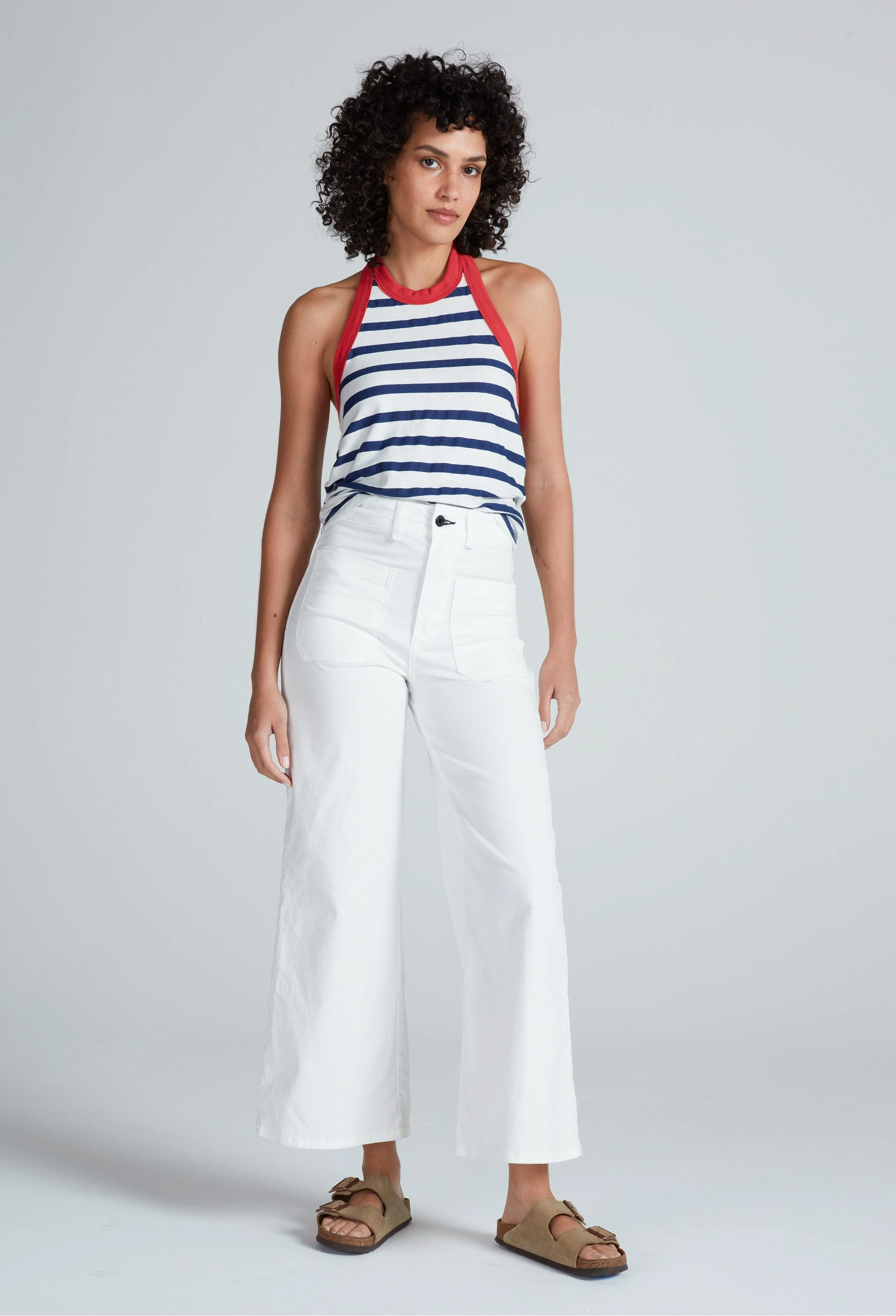 Woman wearing a striped top and white pants on a plain background