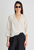 Woman wearing a white blouse and black pants against a plain background