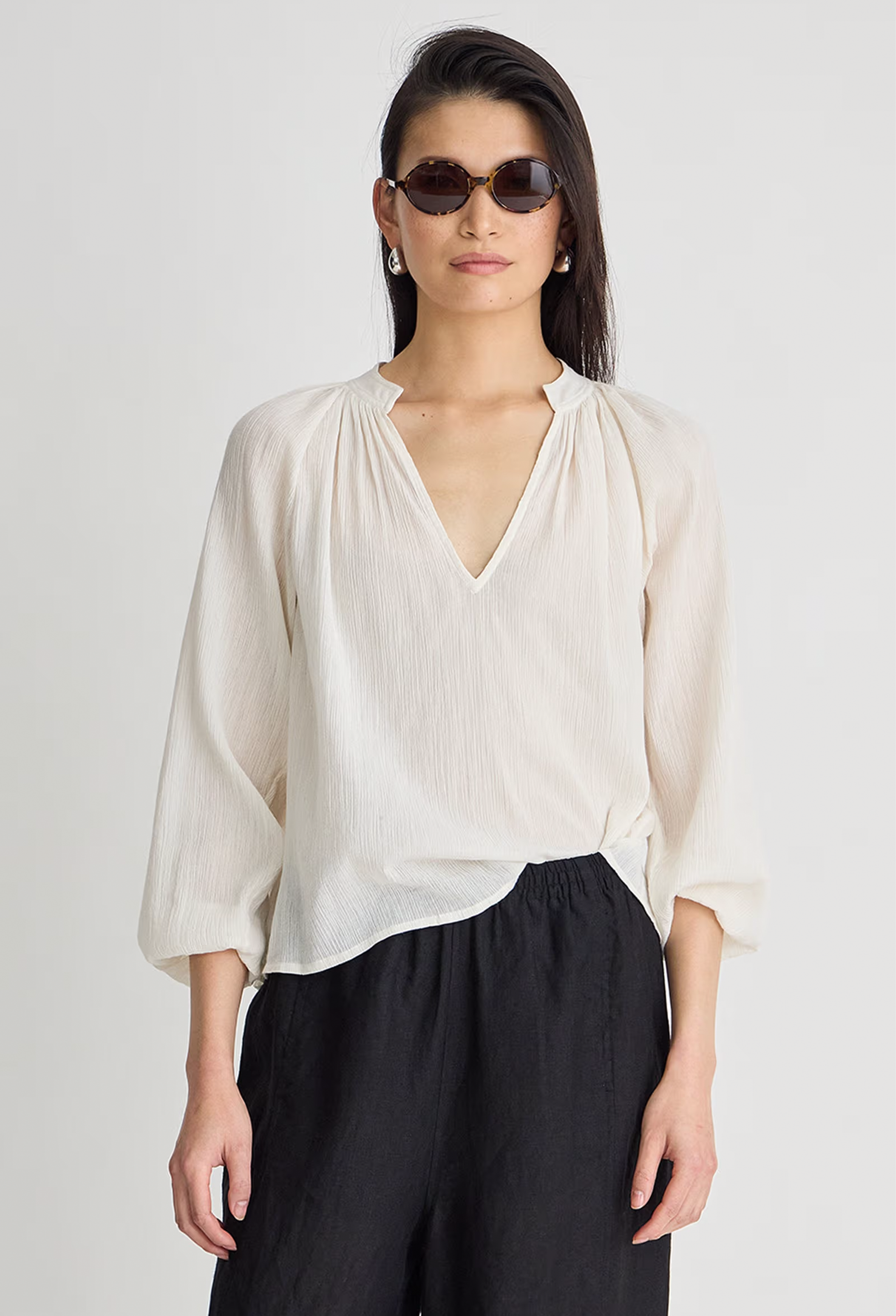 Woman wearing a white blouse and black pants against a plain background