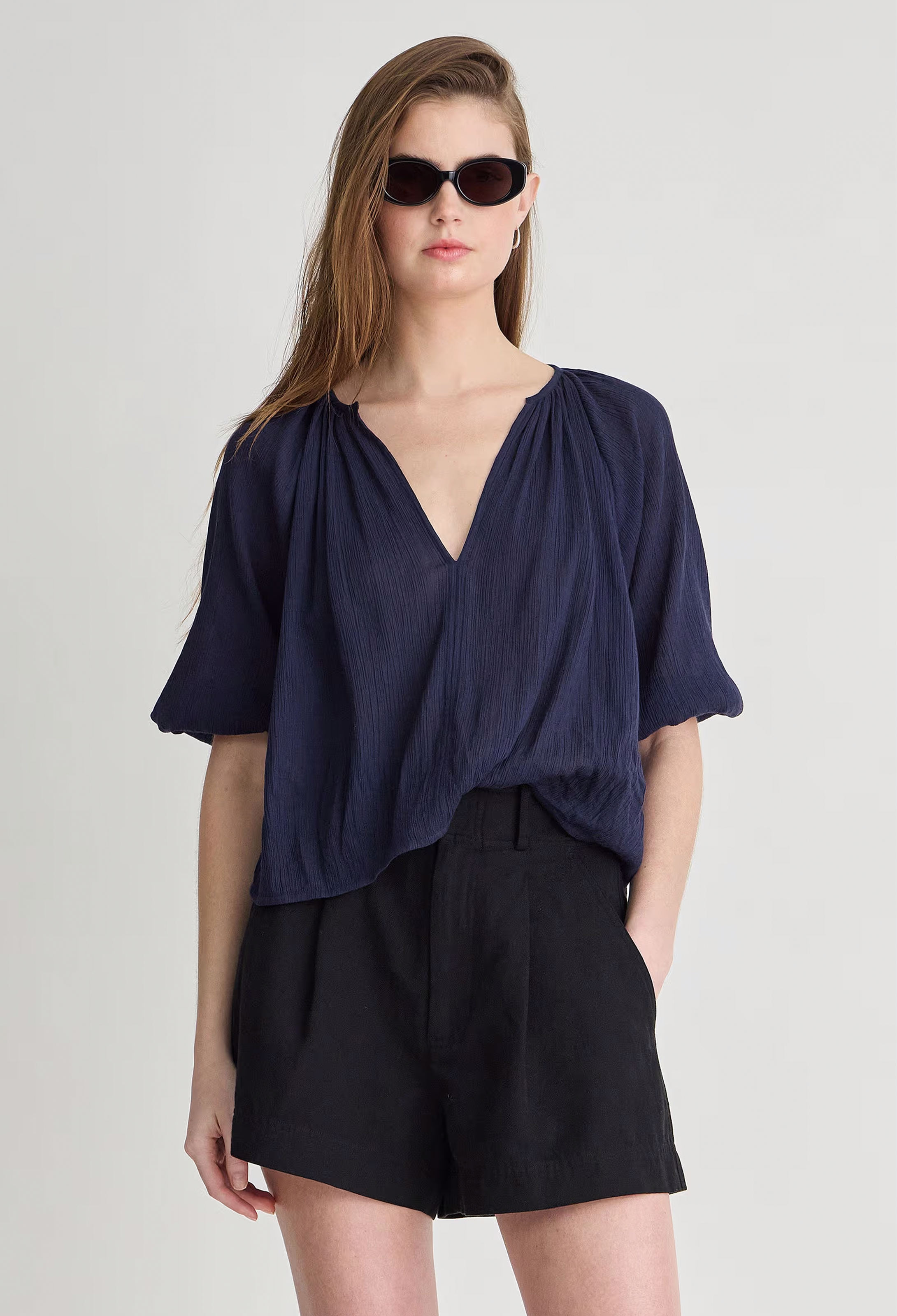 Woman wearing a navy blue top and black shorts on a light gray background