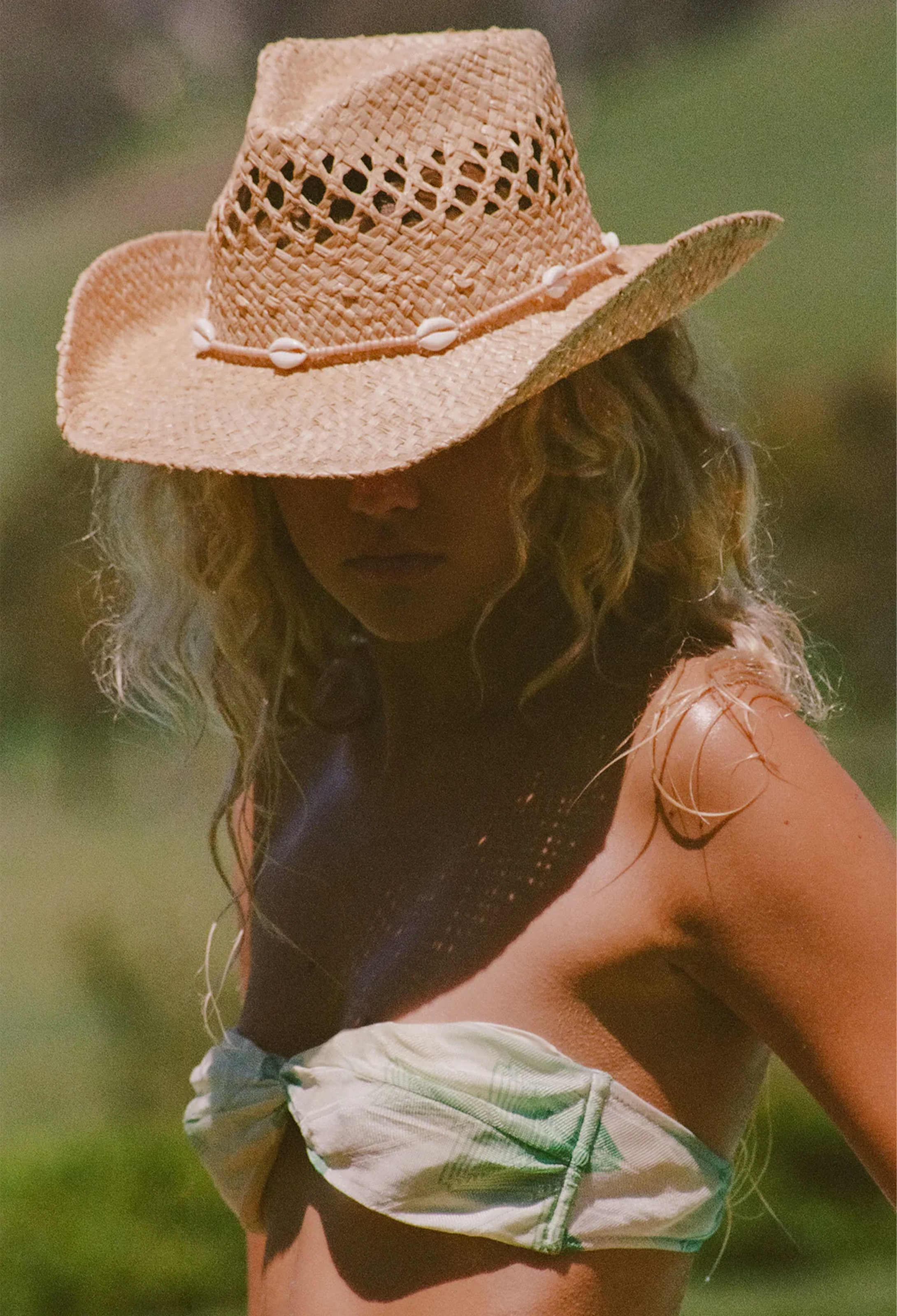 Woman wearing a straw cowboy hat and a green top in a natural setting