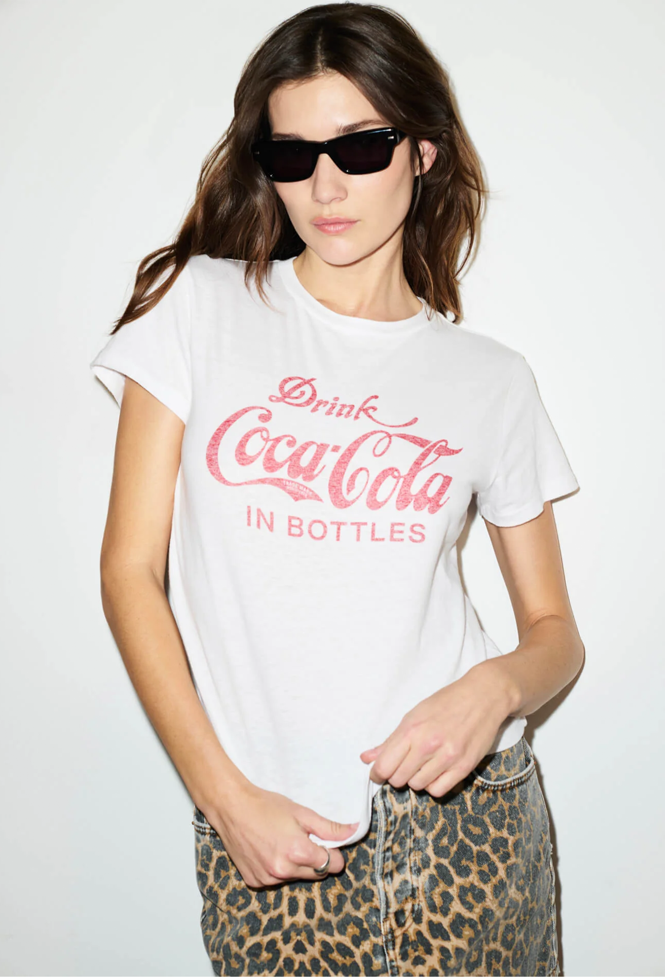 Woman wearing a white t-shirt with red text and leopard print pants on a plain background