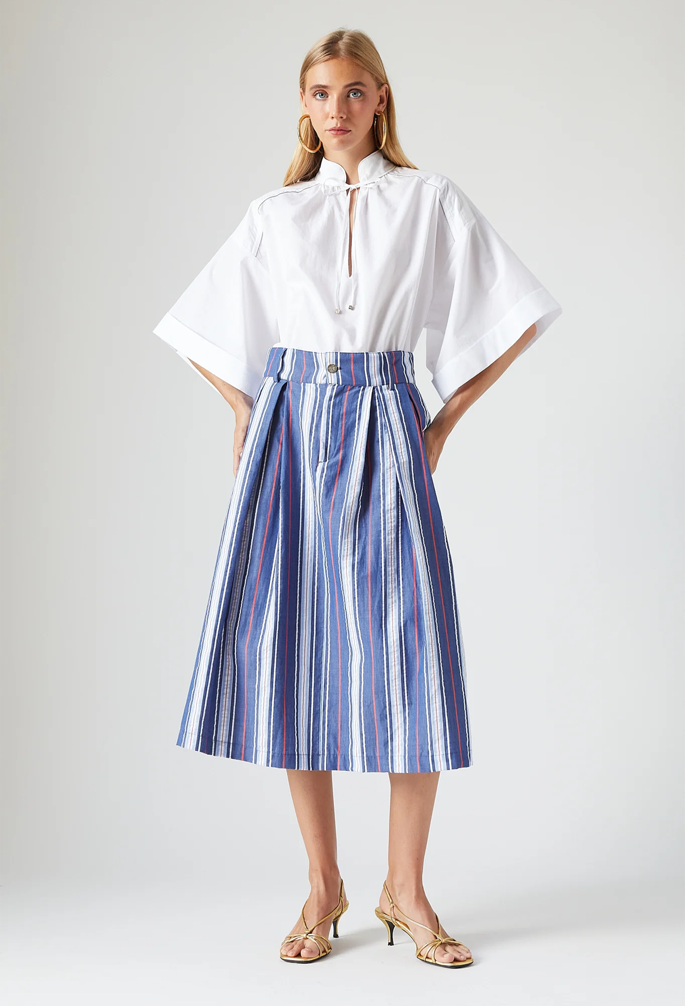 Woman wearing a white blouse and blue striped skirt on a plain background