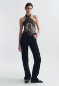 Woman wearing a black halter top with intricate design and black pants on a white background