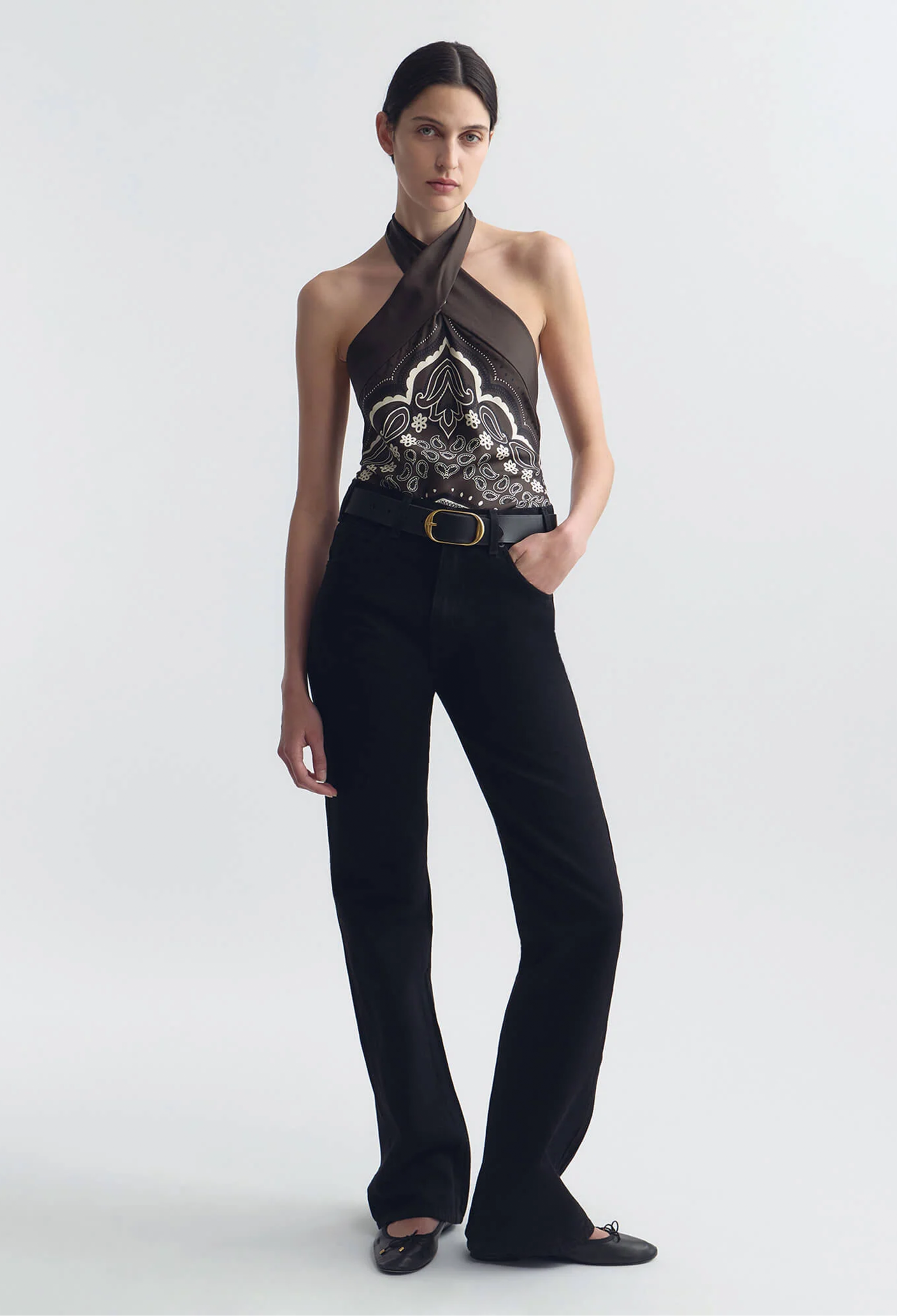 Woman wearing a black halter top with intricate design and black pants on a white background