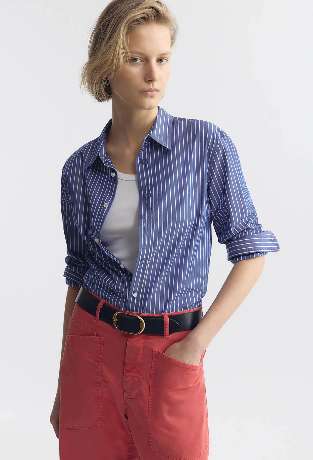 Woman wearing a blue striped shirt, white top, red pants, and black belt on a white background