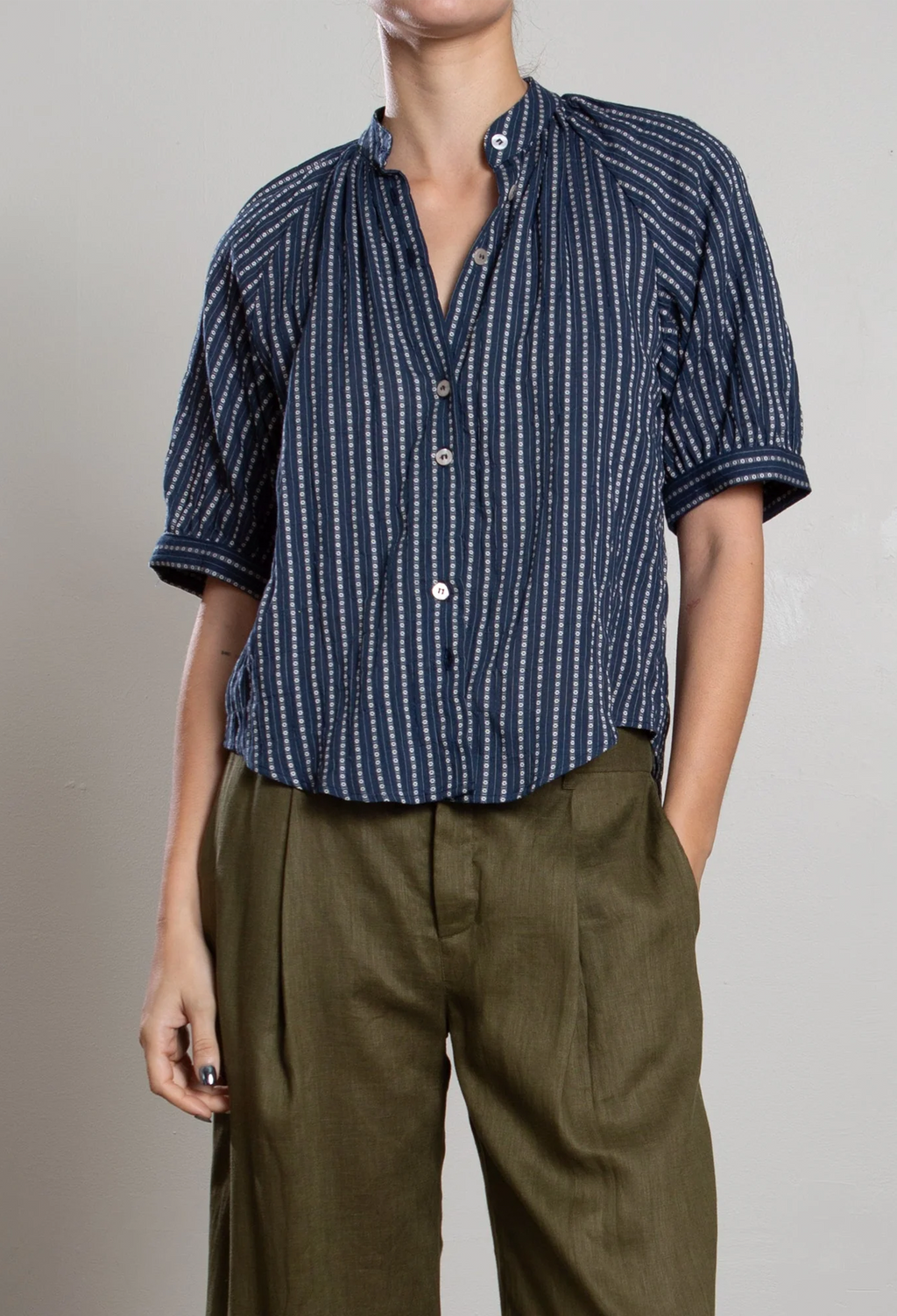 Person wearing a blue patterned shirt and brown pants on a plain background
