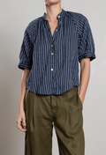 Person wearing a blue patterned shirt and brown pants on a plain background