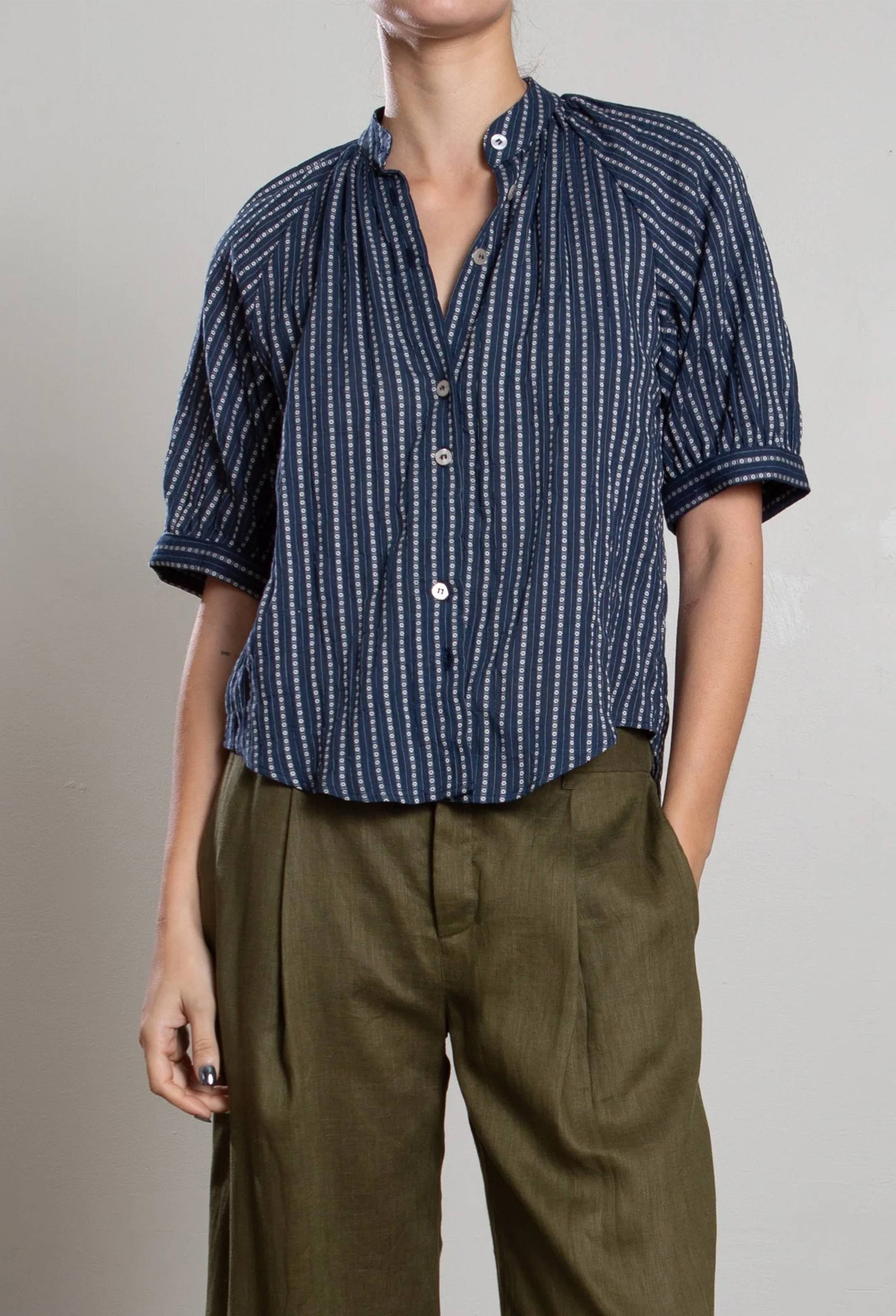 Person wearing a blue patterned shirt and brown pants on a plain background