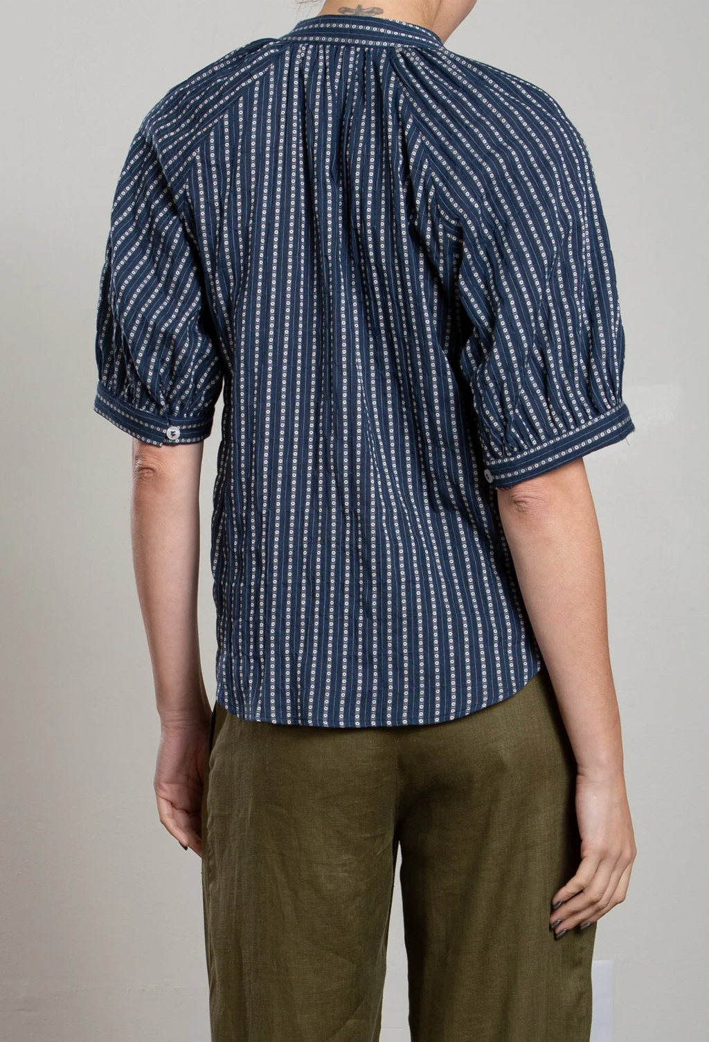 Person wearing a blue and white patterned shirt with green pants on a plain background