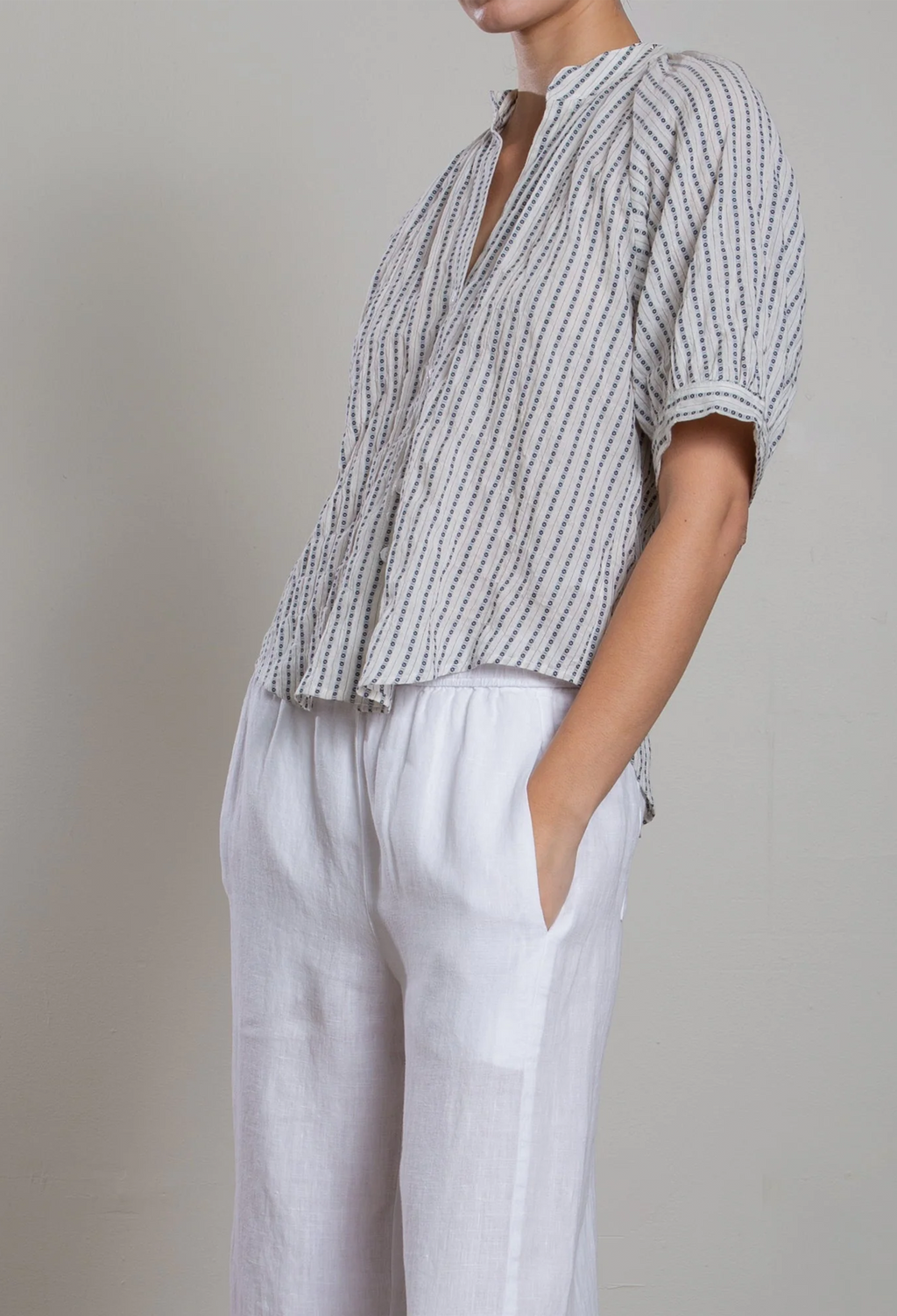 Person wearing a striped shirt and white pants against a plain background