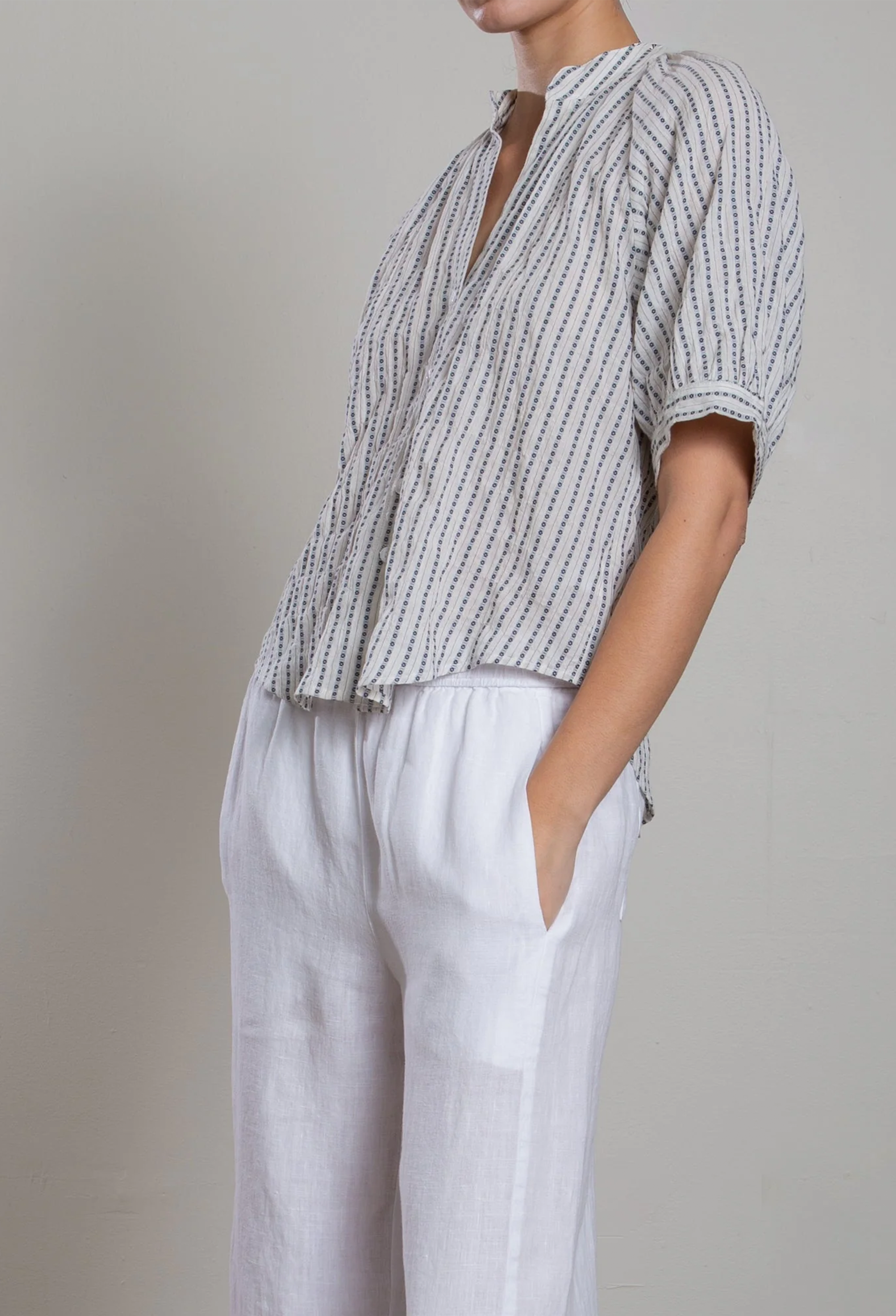 Person wearing a striped shirt and white pants against a plain background