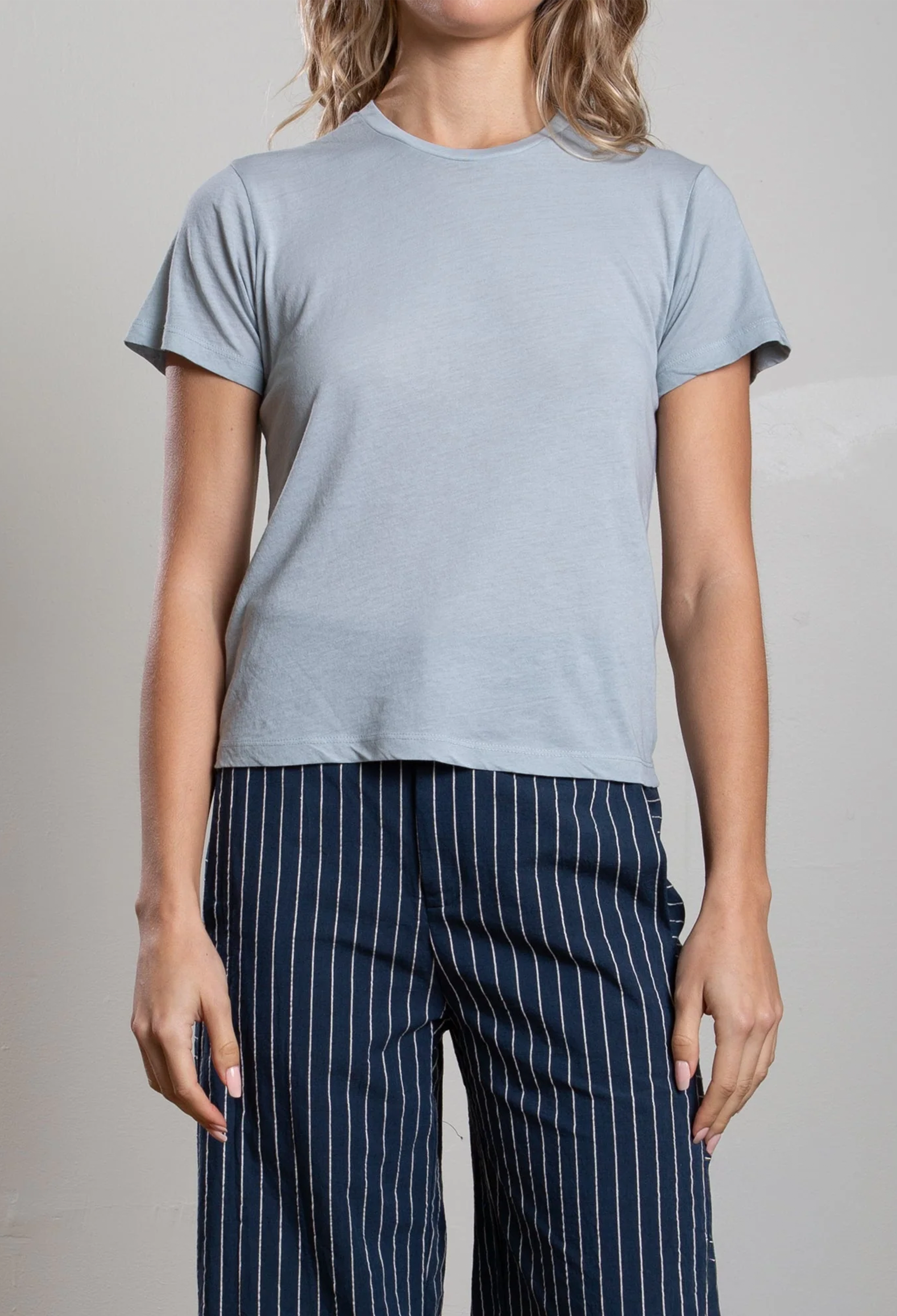 Person wearing a light blue t-shirt and navy pinstripe pants on a neutral background
