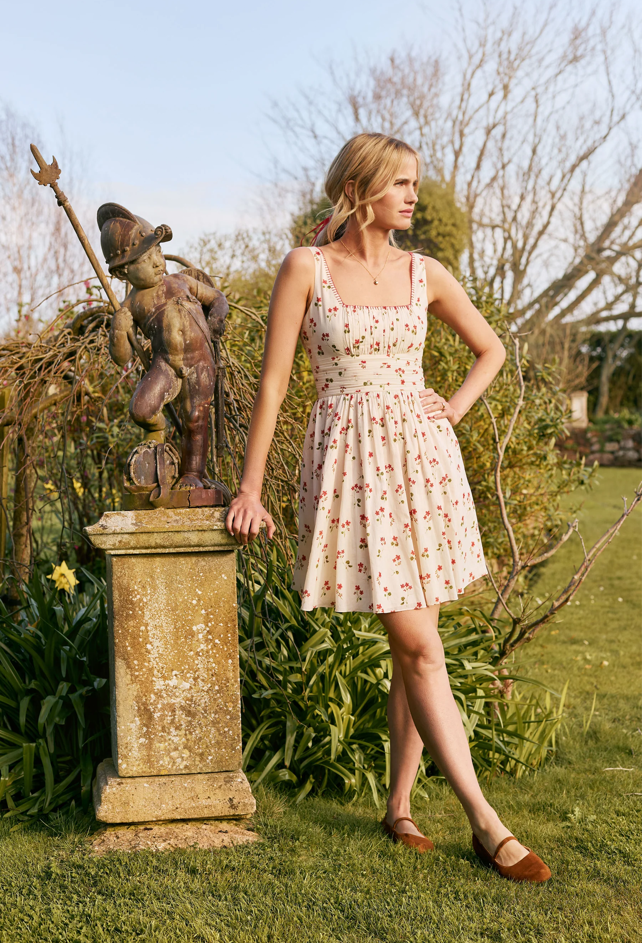 Woman in a floral dress standing next to a statue in a garden