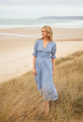 Woman in a blue dress standing on a beach with grass in the foreground