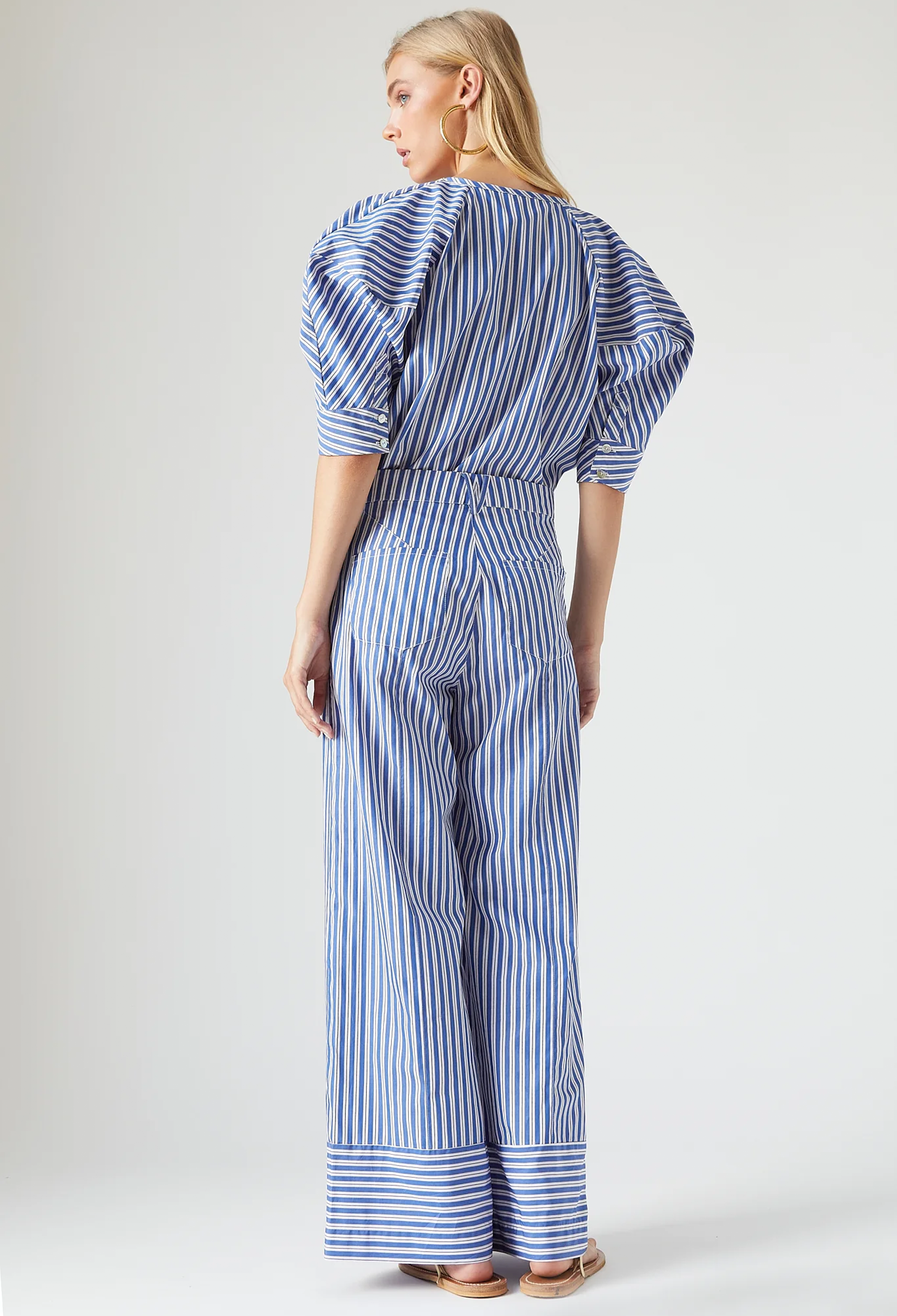 Woman wearing a blue and white striped jumpsuit on a plain background