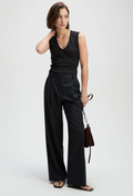 Woman wearing a black sleeveless top and wide-leg pants holding a brown handbag on a white background
