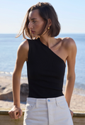 Woman wearing a black sleeveless top and white pants by the ocean.