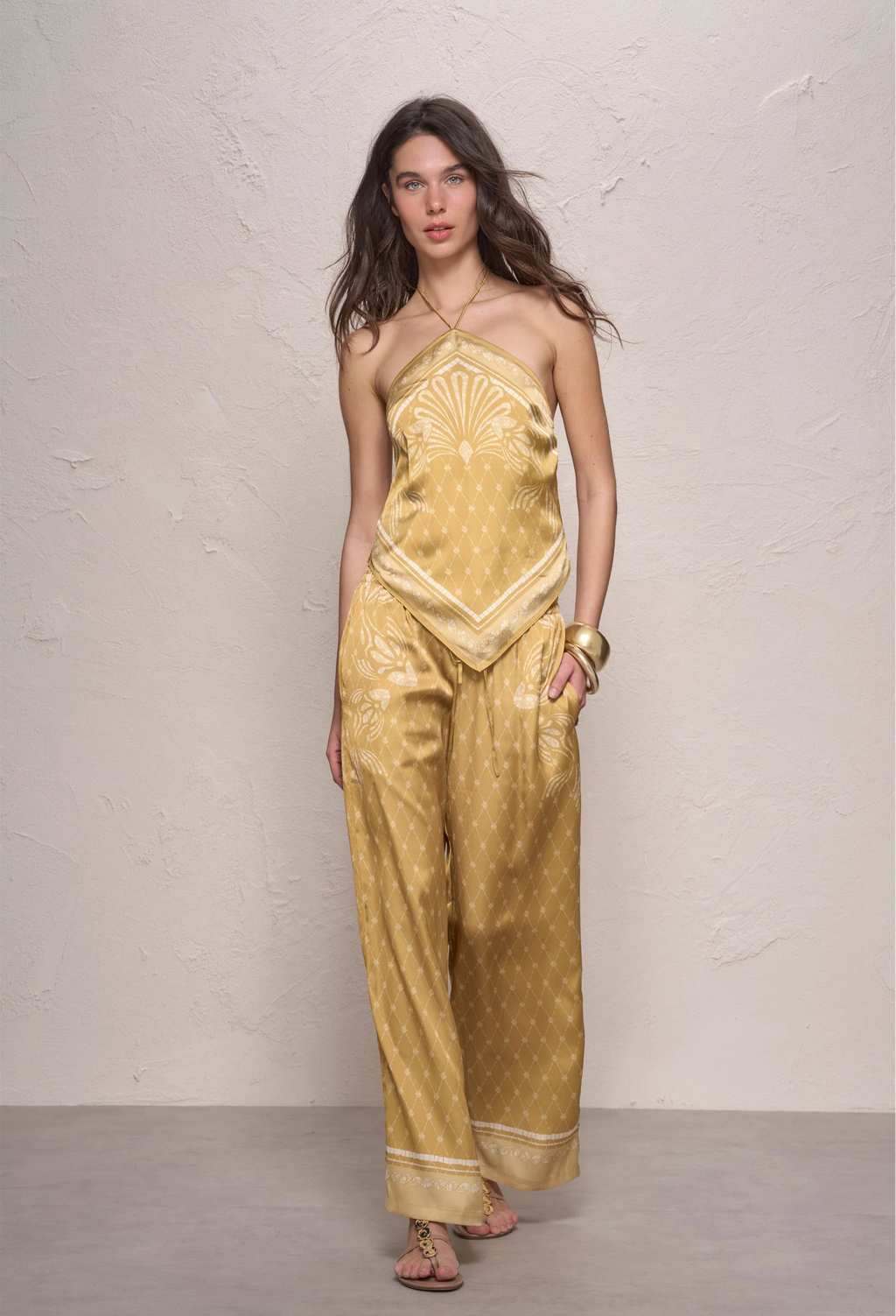 Woman wearing a gold outfit with a textured pattern against a plain background