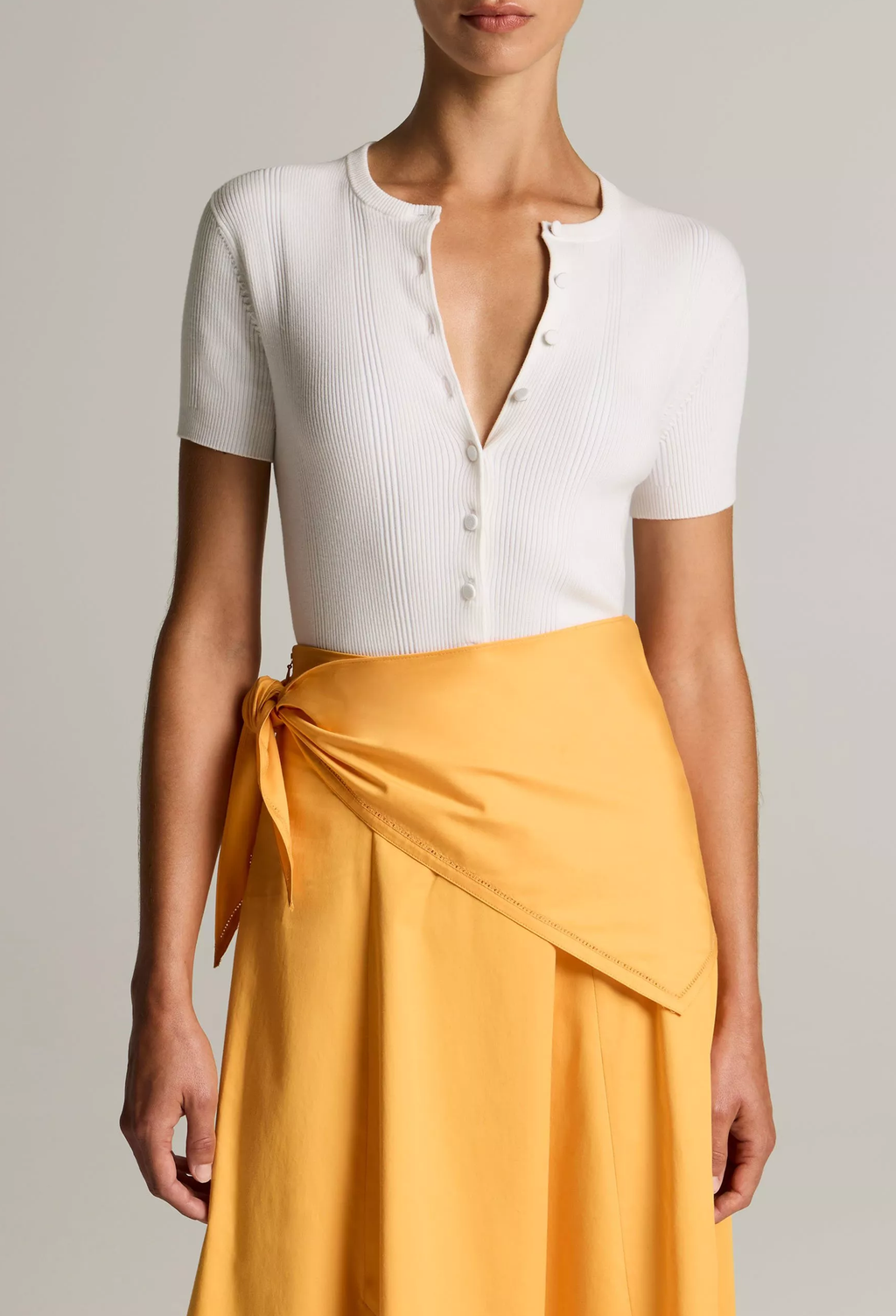 Person wearing a white top and yellow skirt against a neutral background