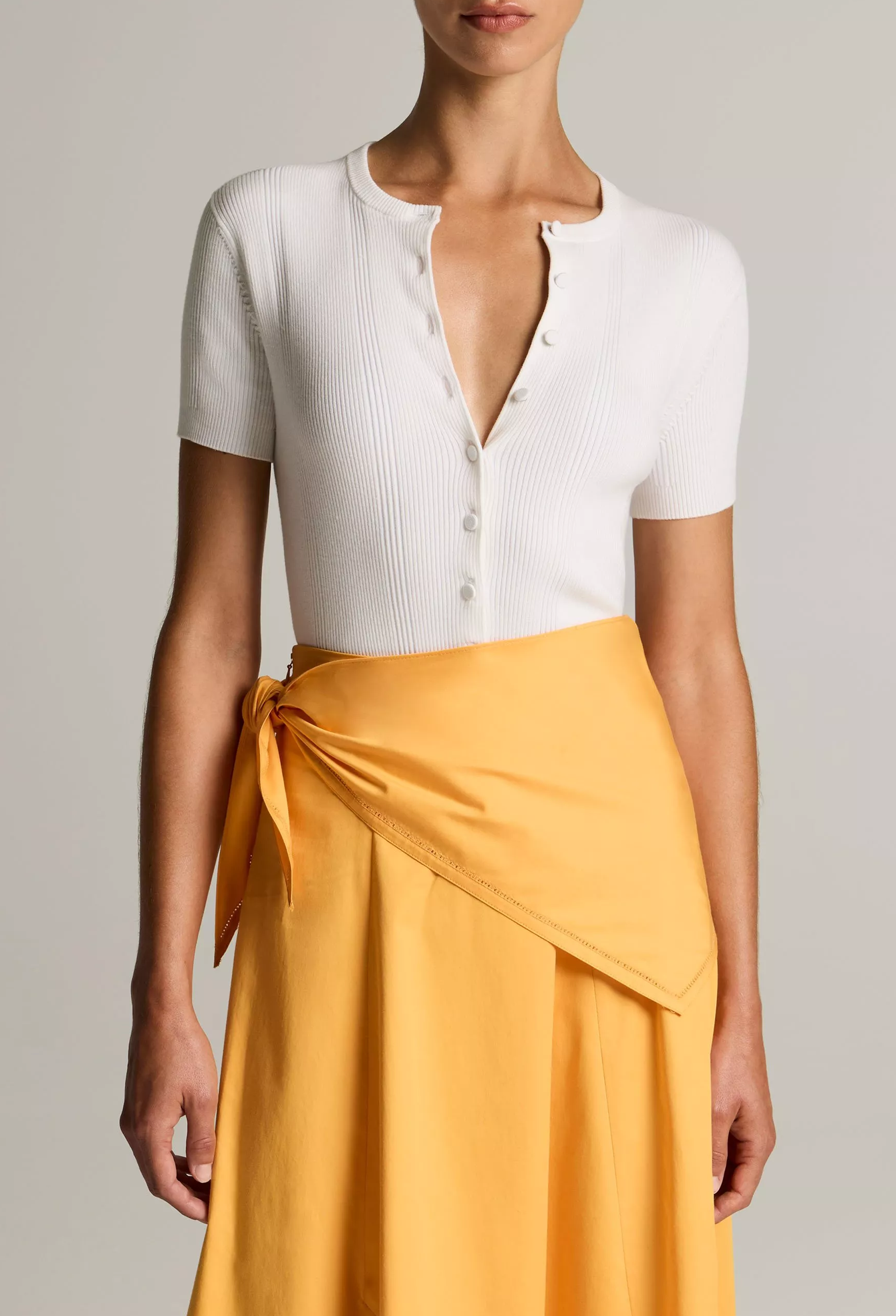 Person wearing a white top and yellow skirt against a neutral background