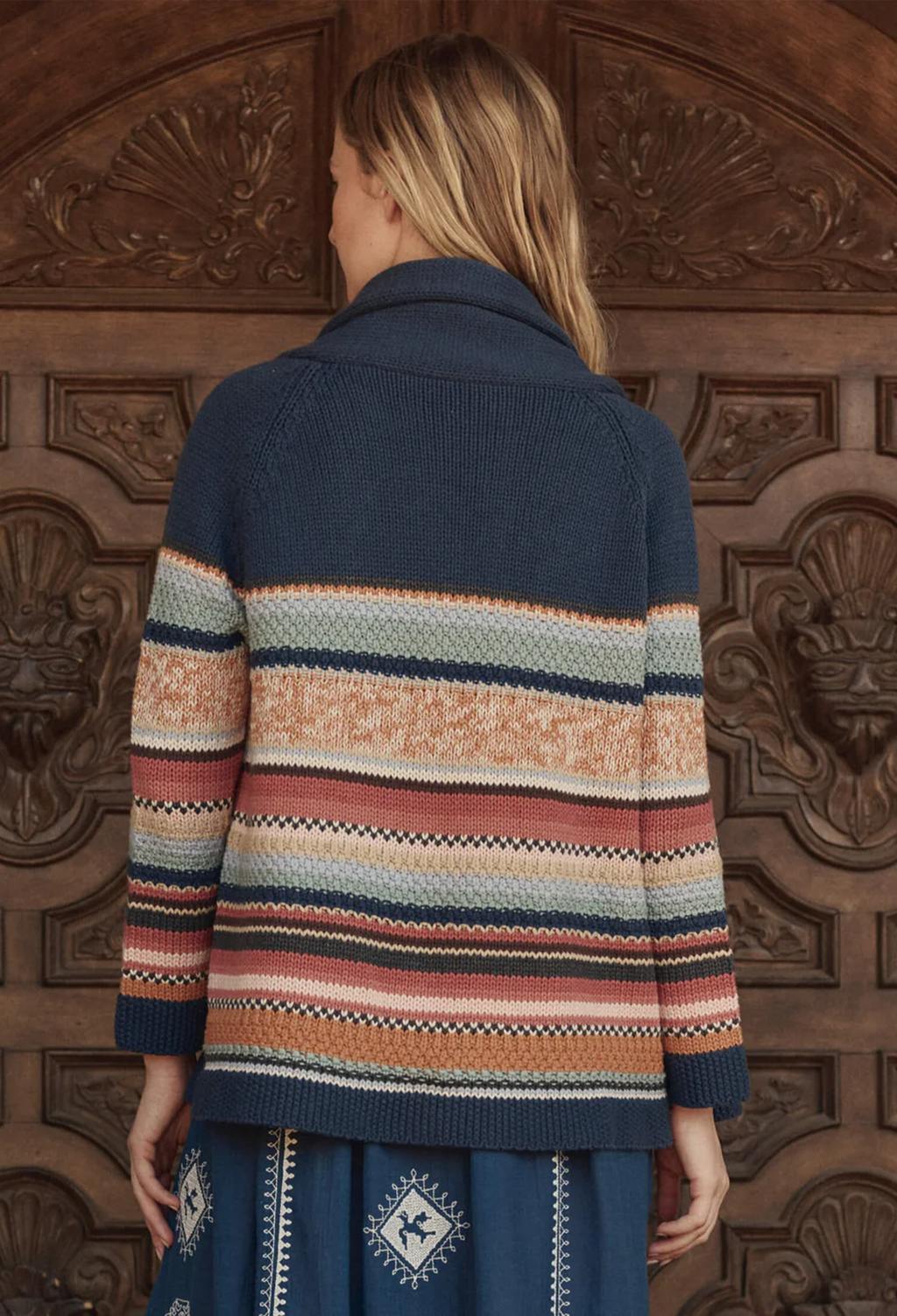 woman wearing a blue multicolored striped cardigan in front of a brown door