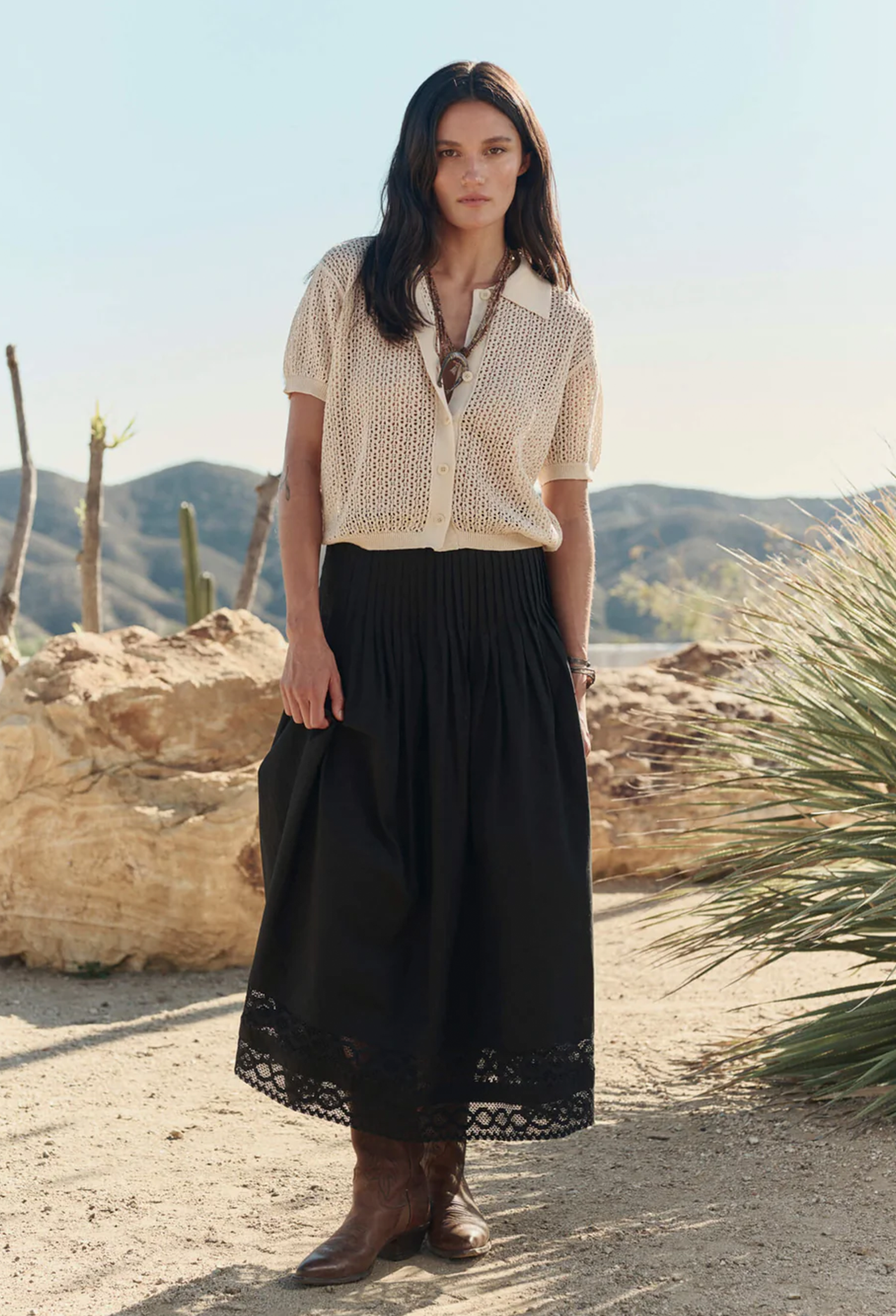 Woman in a white blouse and black skirt standing in a desert landscape with mountains in the background.