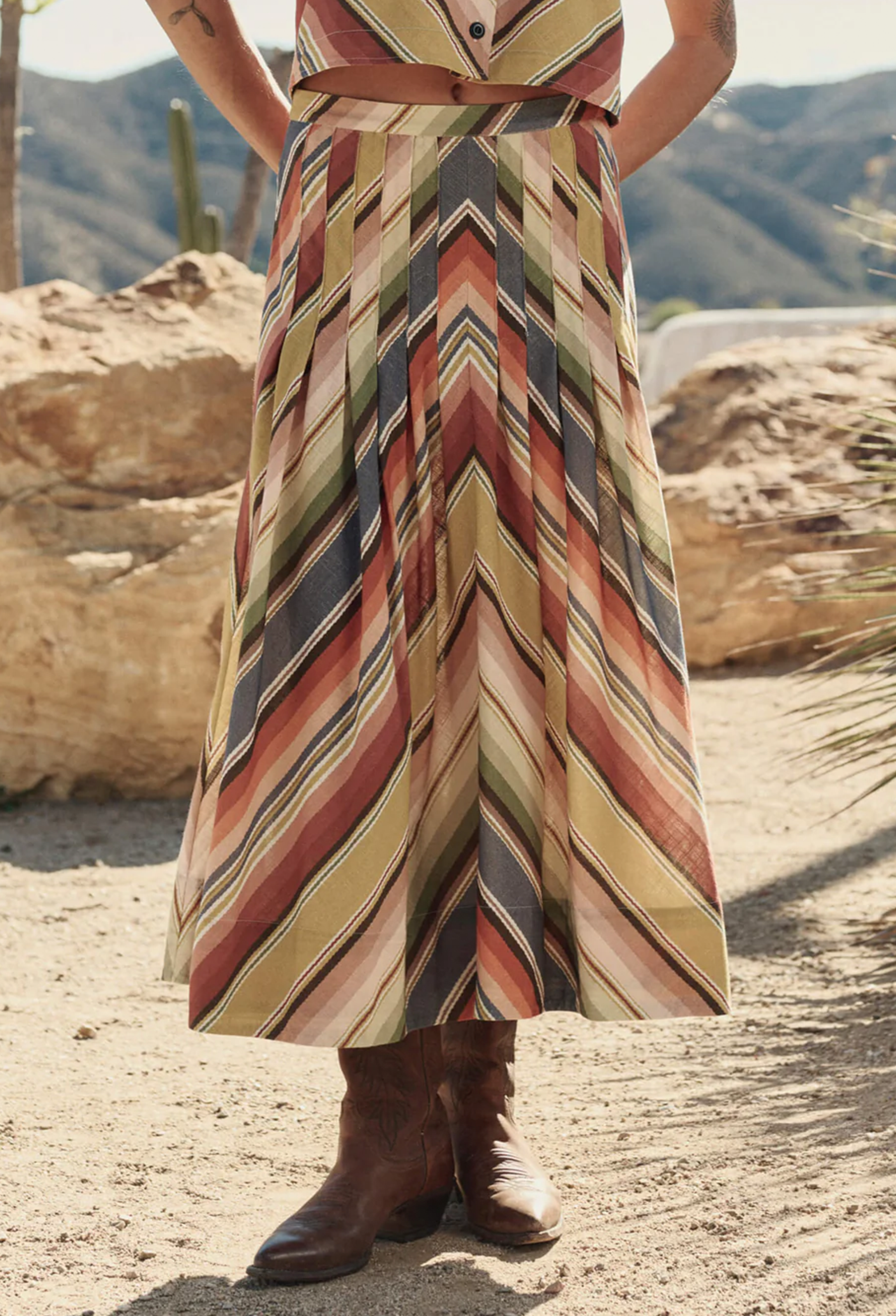 Person wearing a patterned dress standing in a desert landscape with mountains in the background.